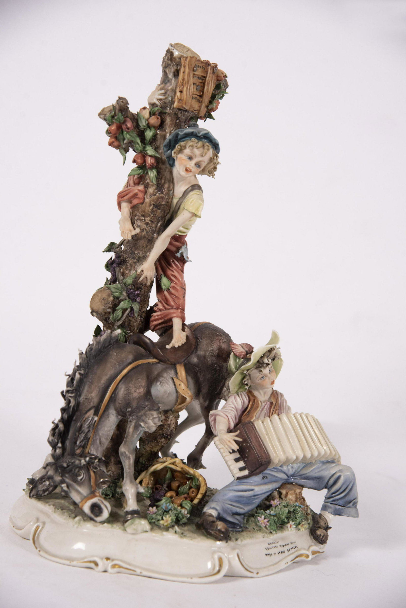 A Large Italian Porcelain Figure Group, Monelli by: A Large Italian Porcelain Figure Group, Monelli by Tiziano GalliThe elaborately sculpted figure of the "Monelli" boys depicting a boy playing an accordion while the other boy climbs a fruit