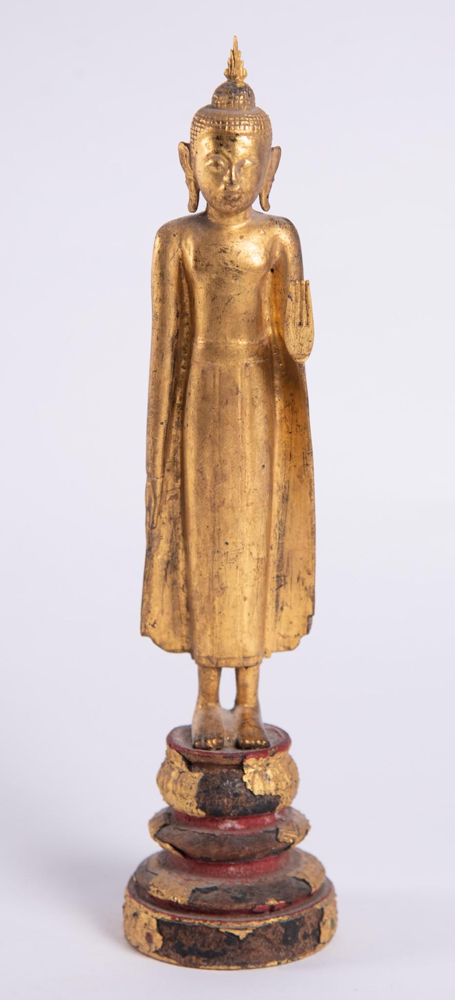 An Antique Gilt Wood Buddha: An Antique Gilt Wood Buddha A diminutive carved Thai Buddha with outstretched hand, standing atop a lotus plinth. 14" tall Imperfections and losses to gilding on base