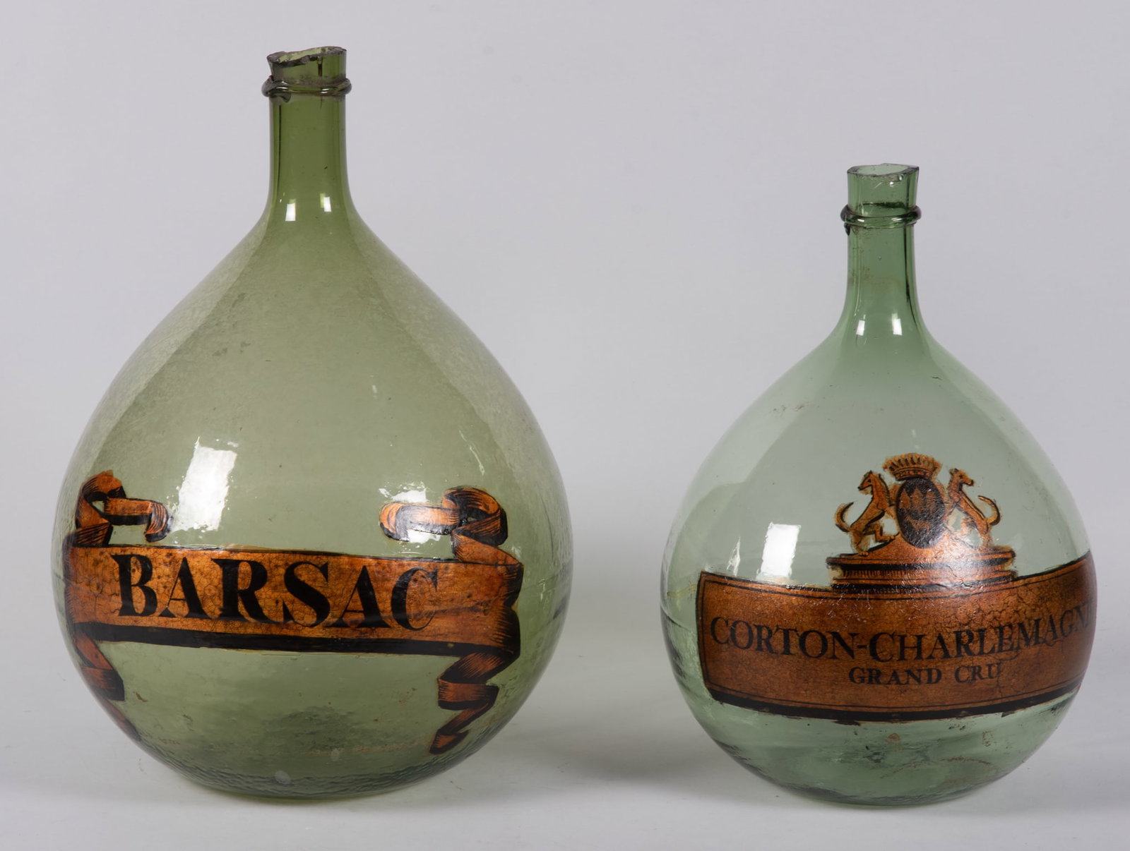 Pair of Vintage Green Glass Demijohns with Labels: Pair of Vintage Green Glass Demijohns with Labels Nice pair of vintage green glass demijohns wine holders. Each having different heights and applied labels of gold and black indicating the contents. M