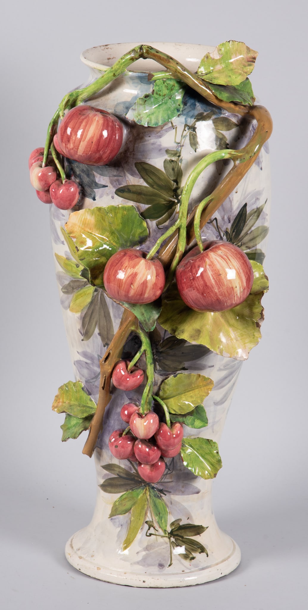 Tall French Majolica Urn with Applied Fruit: Tall French Majolica Urn with Applied Fruit Tall French tin glazed majolica urn with a white and floral background and ceramic vines with leaves and apples and cherries applied to the front side of th