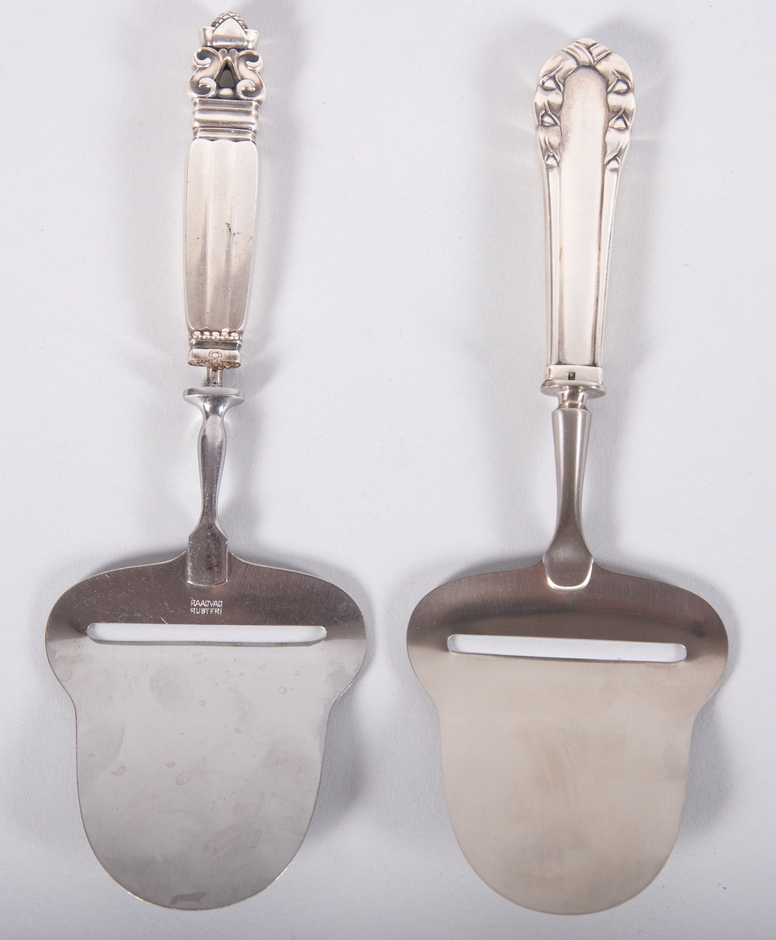 Two Vintage Georg Jensen Sterling Silver and Stainless Steel Cheese Planes: Two Vintage Georg Jensen Sterling Silver and Stainless Steel Cheese Planes One Acorn design, the other Lilly of the Valley; both with sterling silver handle and stainless steel blade, marked; total we