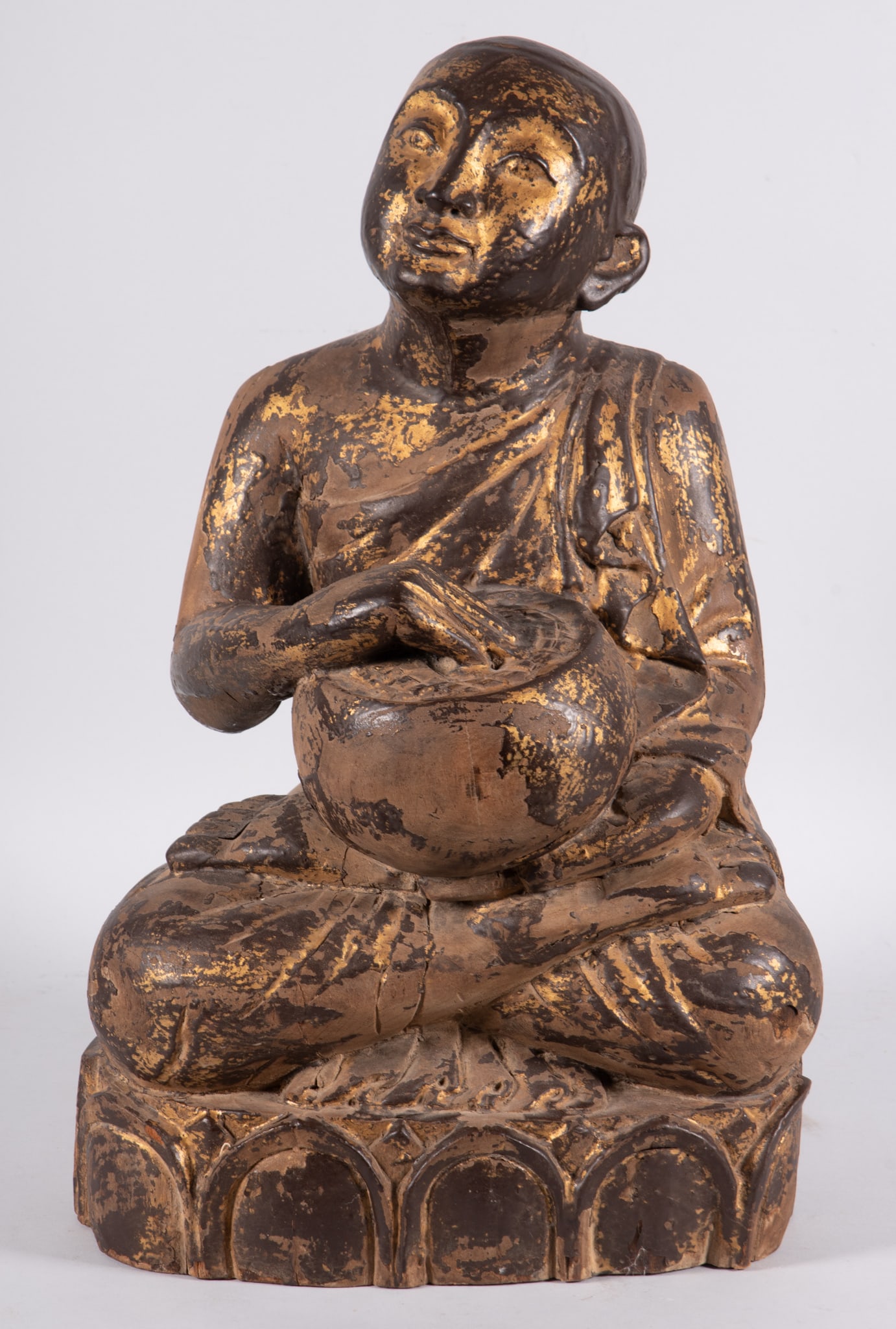 A Carved and Parcel Gilt Wood Buddhistic Sculpture: A Carved and Parcel Gilt Wood Buddhistic SculptureDepicting a serene young monk seated atop a lotus with a ceremonial drum in his lap. 21 1/2 inches tall, 13 inches wide.