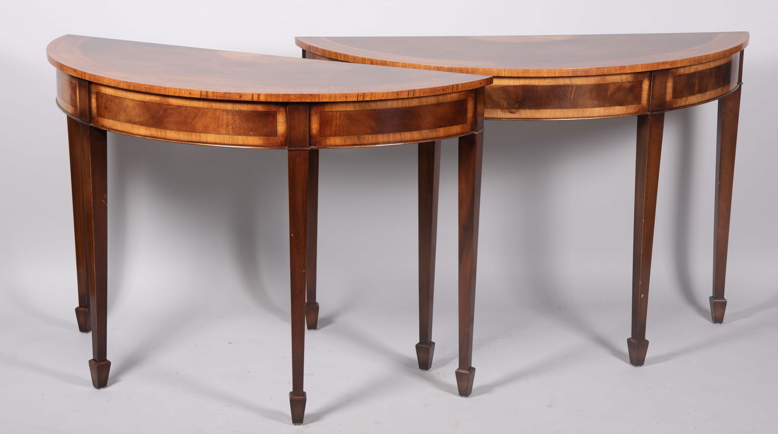 Trosby Furniture Company, Pair Of Satinwood Modern Console Tables: Trosby Furniture Company, Pair Of Satinwood Modern Console TablesDemi lune tops with crossbanding and shell form decoration above crossbanded aprons raised on tapering legs and spade feet.32 x 19 x 42