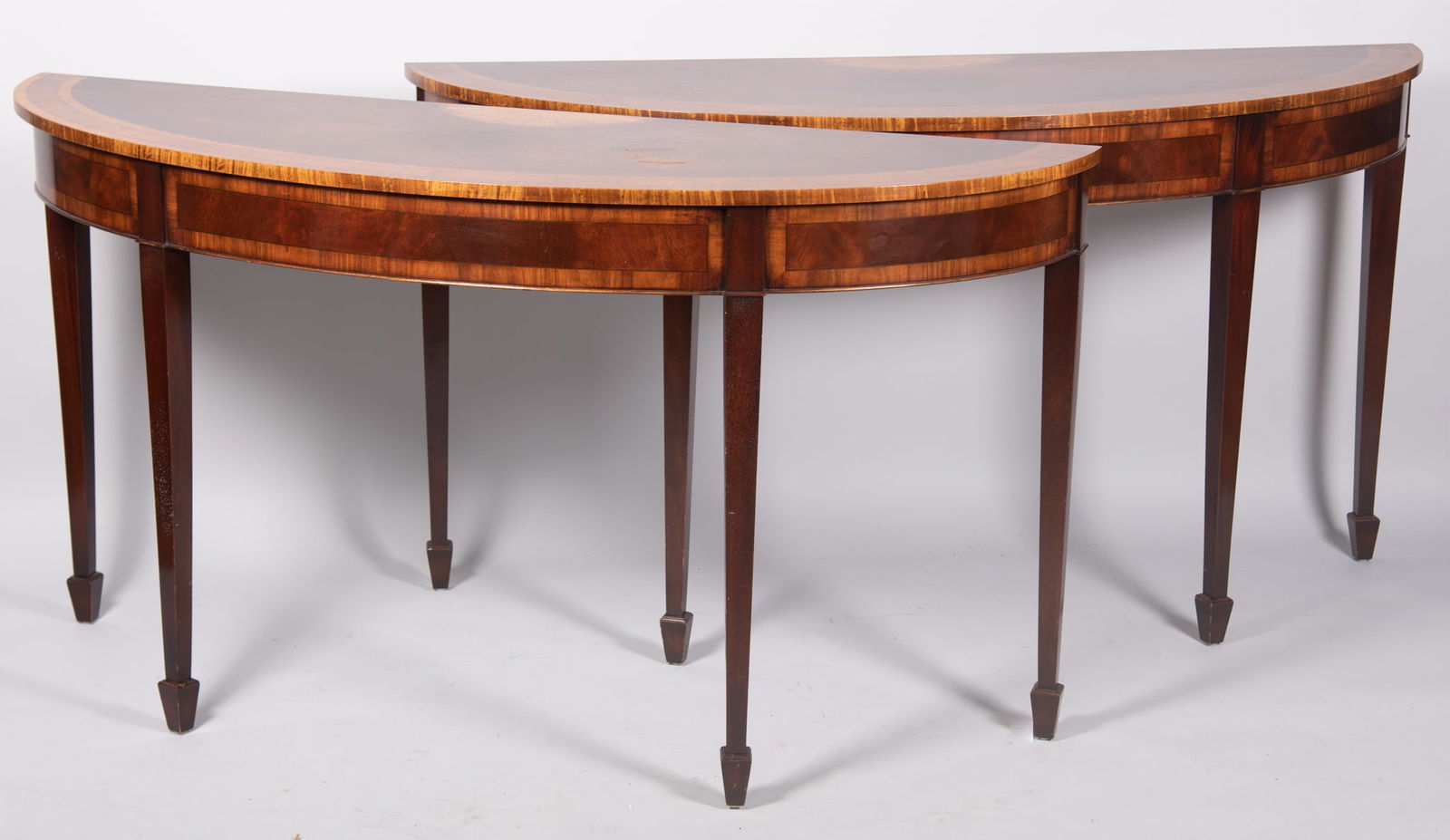 Trosby Furniture Company, Pair Of Satinwood Modern Console Tables: Trosby Furniture Company, Pair Of Satinwood Modern Console TablesDemi lune tops with crossbanding and shell form decoration above crossbanded aprons raised on tapering legs and spade feet.32 x 60 x 19
