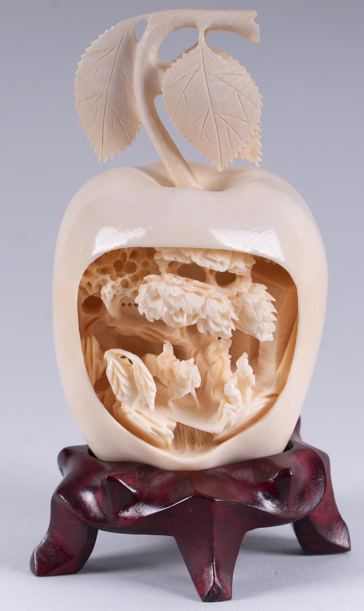 A Japanese Carving of an Apple with an Internal Village Scene: A Japanese Carving of an Apple with an Internal Village Scene A 4 1/2 inch tall study of an apple with an intricately carved village scene portraying multiple figures and a horse against a rocky lands