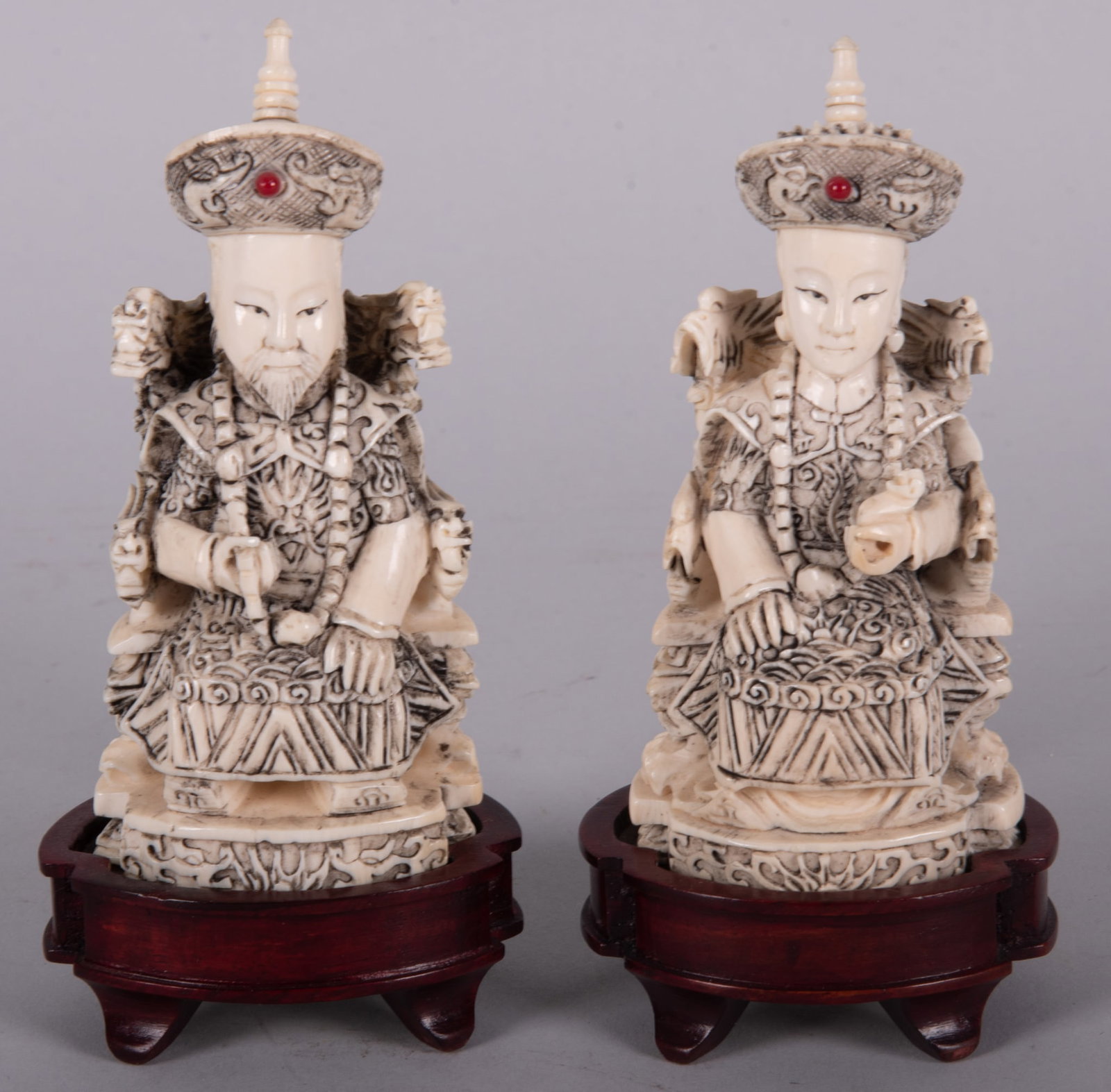 A Pair of Chinese Carved Bone Figures, Emperor and Empress: A Pair of Chinese Carved Bone Figures, Emperor and Empress A diminutive pair of seated figures in throne chairs, each with a red "jewel" in their crown. Total height in fitted wood stands 5 
