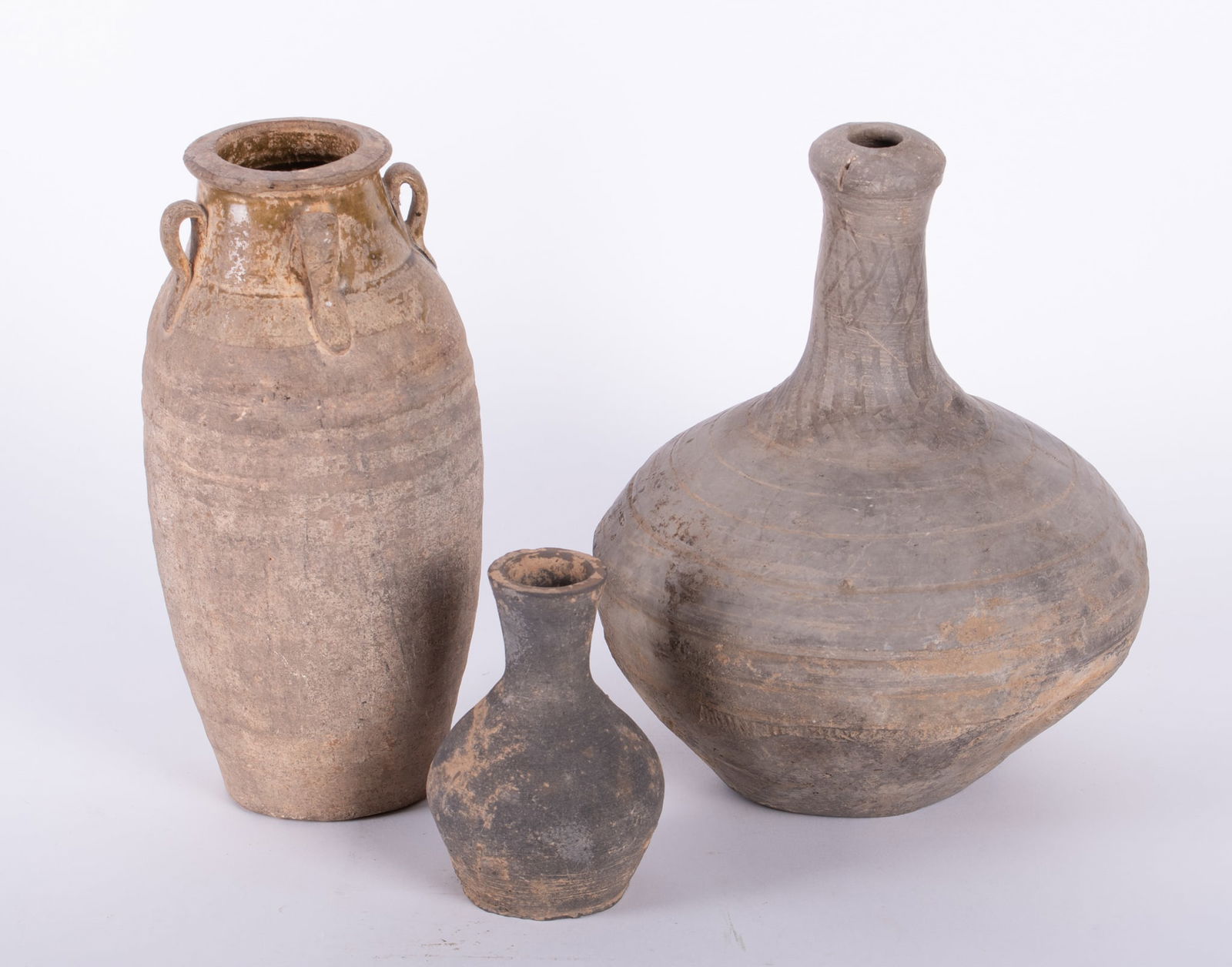 Three Antique Earthenware Vessels, likely Chinese: Three Antique Earthenware Vessels, likely ChineseAn amphora vase having ovoid shaped body with four looped handles, still bearing some of the original green glaze and concentric impressions about the