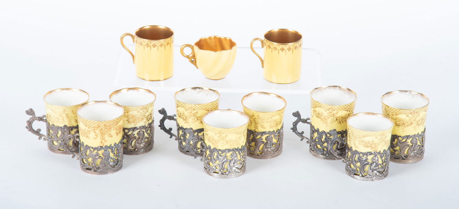 Nine Sterling Silver and Porcelain Demi-Tasse Cups, Circa 1886: Nine Sterling Silver and Porcelain Demi-Tasse Cups, Circa 1886 England, circa 1886, the set of yellow ground Staffordshire porcelain cups having gilt highlights, being held in sterling silver rococo