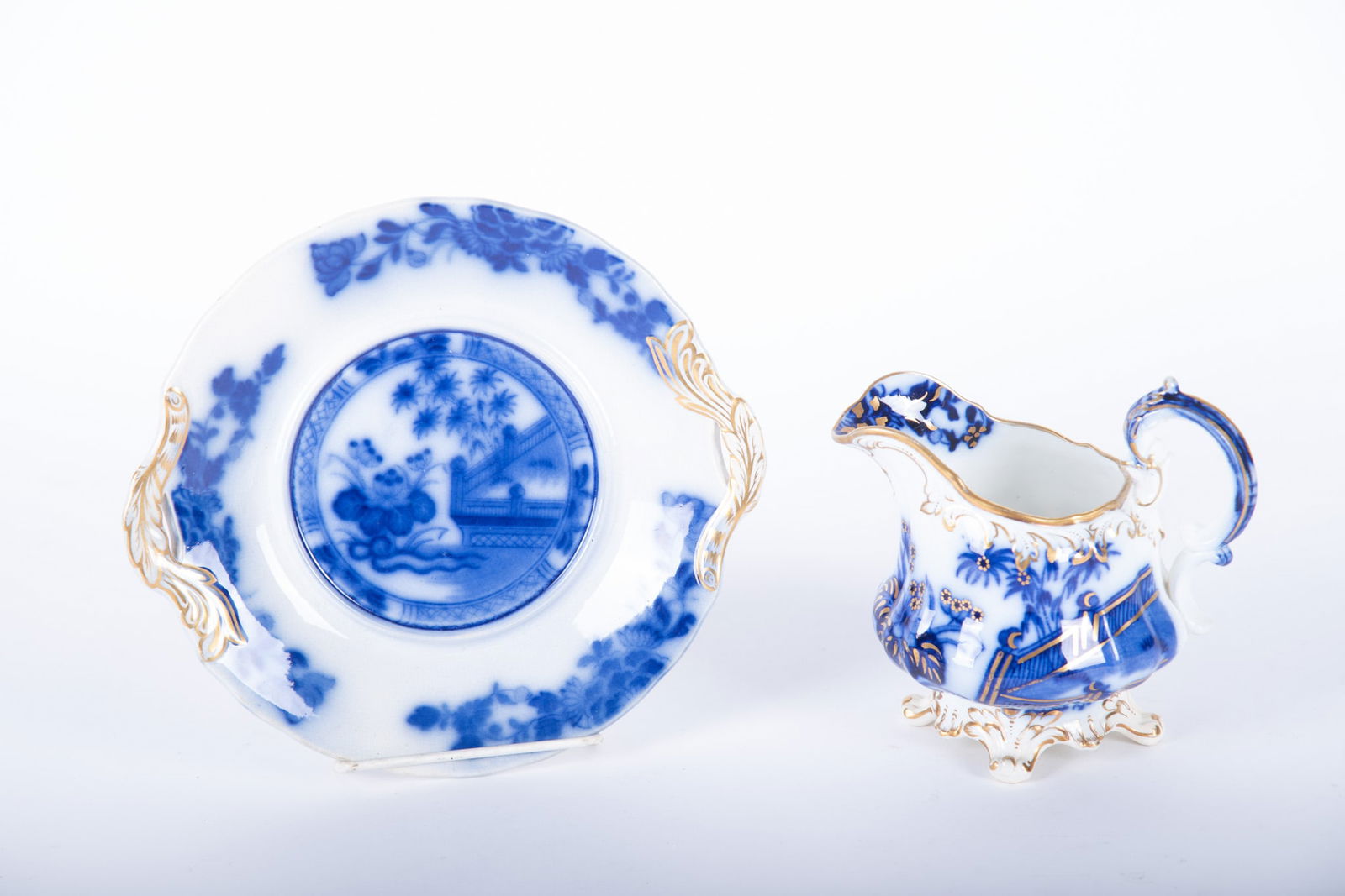 An Antique Flow Blue Serving Creamer and Underplate, Oriental by Samuel Alcock and Sons: An Antique Flow Blue Serving Creamer and Underplate, Oriental by Samuel Alcock and Sons Staffordshire England, an associated gold "clobbered" creamer with similar handled underplate, both in the
