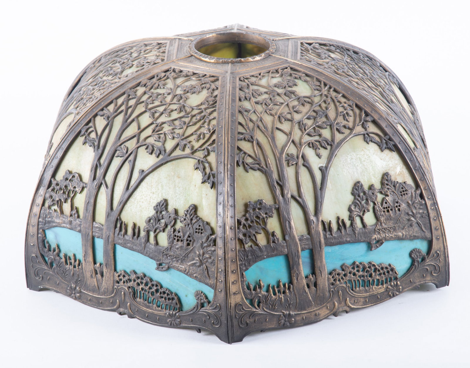 An Antique Art Nouveau Metal Overlay Slag Glass Lamp: An Antique Art Nouveau Metal Overlay Slag Glass LampAmerican, early 20th century, likely Miller or Bradley and Hubbard, the shade constructed of a patinated metal cage depicting a scenic landscape of