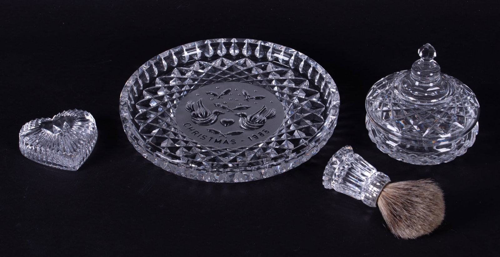 Four Waterford Crystal Objects: Four Waterford Crystal Objects The lot includes a heart shaped paperweight, a bristle shaving brush, a covered 4 inch diameter dish with cut finial, and a Christmas 1986 round dresser tray. Tray: 8