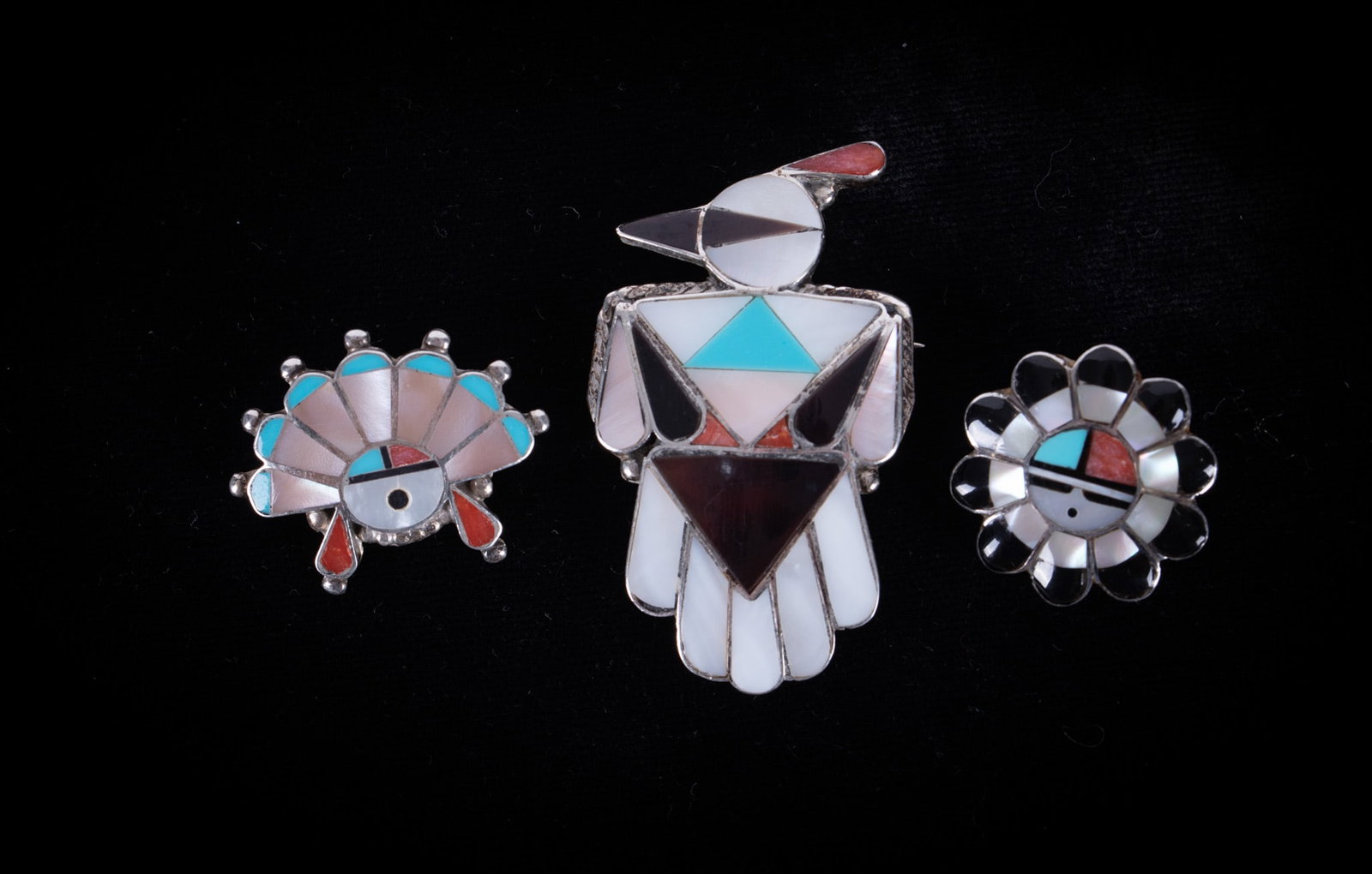 Three Vintage Zuni Brooches/Pendants: inset with mother-of-pearl, black onyx, turquoise and coral; two are a face pin/pendant and one is a Thunderbird; sterling silver mounts; sizes 1 1/2 x 1 inch, diameter 3/4 inch, width 1 inch.