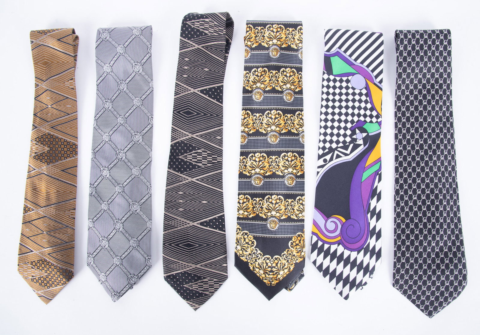 Group of Six Gianni Versace 100% Silk Designer Ties: one contemporary black and white geometric with green and purple design, marked V2 By Versace; one grey/silver triangle pattern, Made in Italy; one gold tone with brown/black geometric pattern, marked