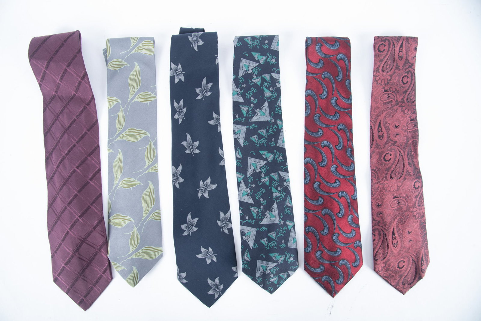 Group of Six Giorgio Armani Silk Designer Ties/Cravatte: one light Maroon with cornucopia design, marked Made In Italy; one dark Maroon with blue/black curved design, Made in Italy; one black background with grey/green spheres, Made in Italy; one black