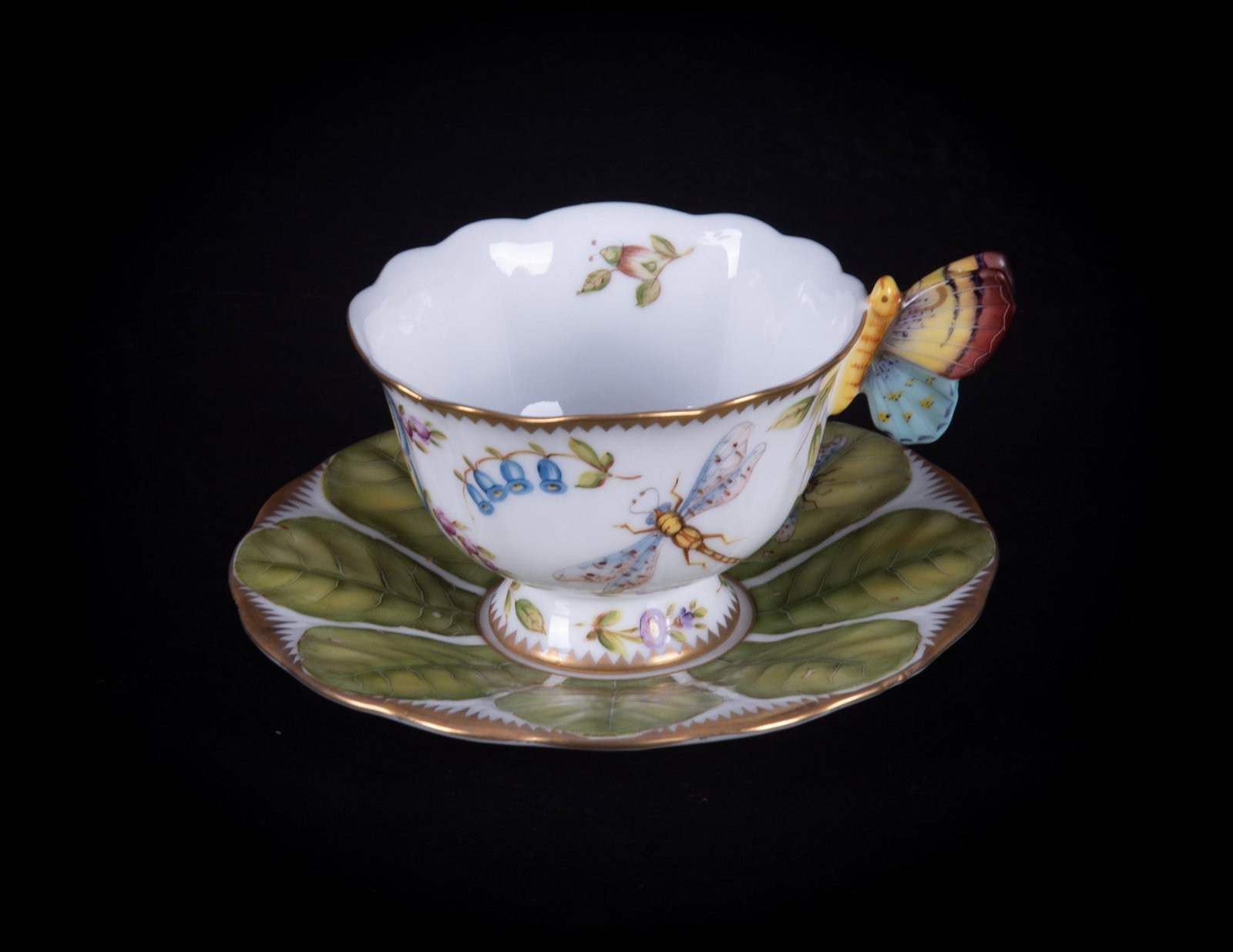An Anna Weatherley Porcelain Butterfly Handle Cup and Saucer: Hungary, a difficult to find butterfly handle cup and saucer by Anna Weatherley Designs. The body with bluebells and other botanicals, a butterfly, a dragonfly, and a grasshopper. The leaf pattern sau