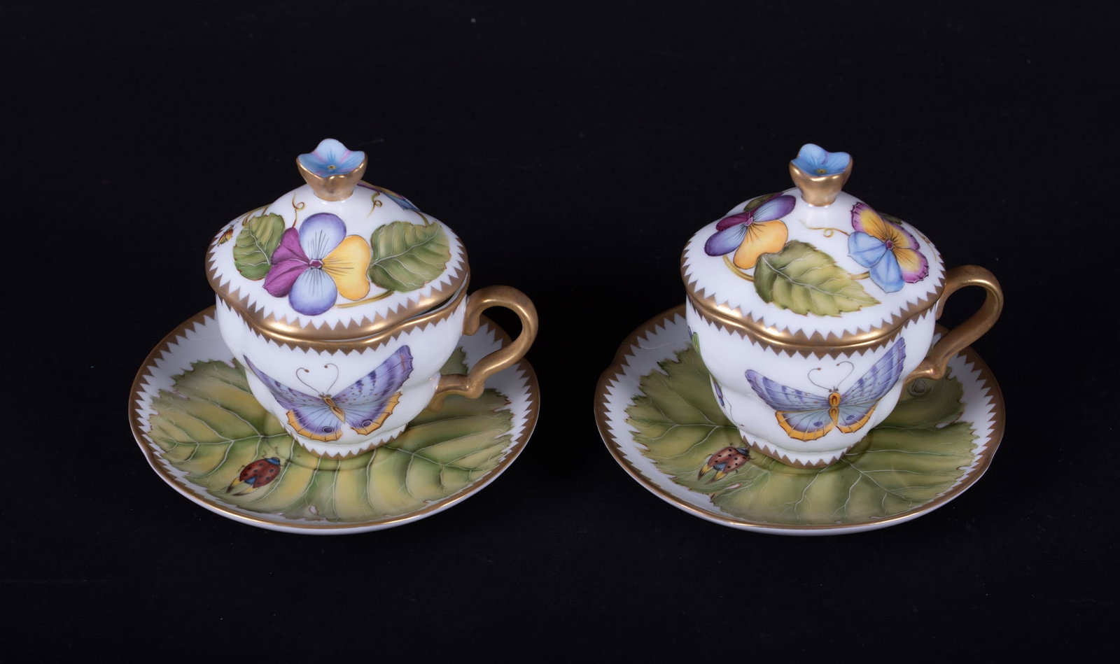A Pair of Anna Weatherley Covered Chocolate Cups and Saucers: Hungary, a difficult to find set of chocolate or espresso lidded cups and saucers, the body of the cups having a butterfly, moth, and dragonfly, the lids with botanicals and bugs, the saucers with lar