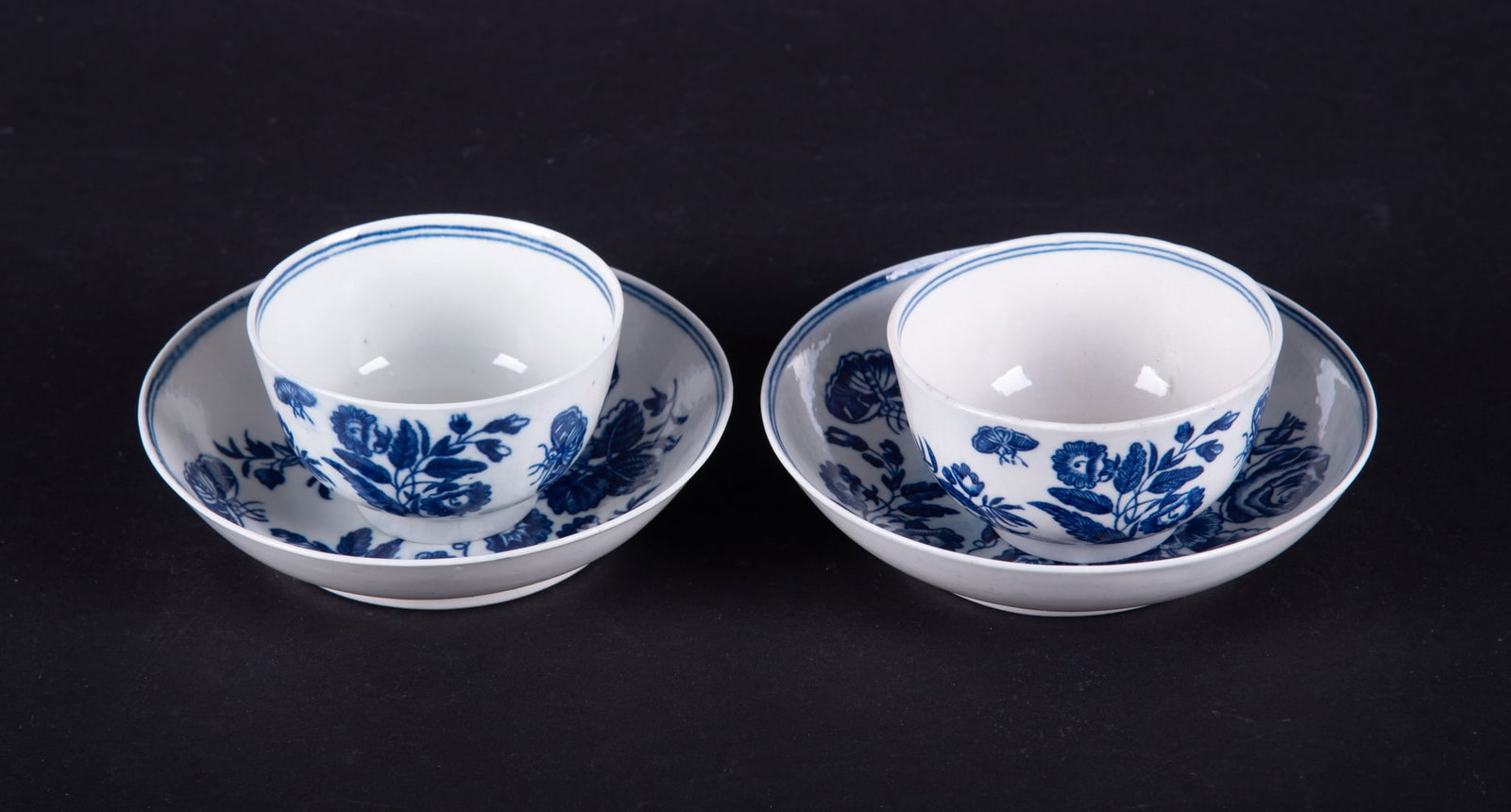 A Near Pair of 18th Century Worcester Cups and Saucers, Three Flowers: England, circa 1780, Dr. Wall period tea cups and saucers with butterflies amidst floral scenes, bearing blue crescent mark to base.
