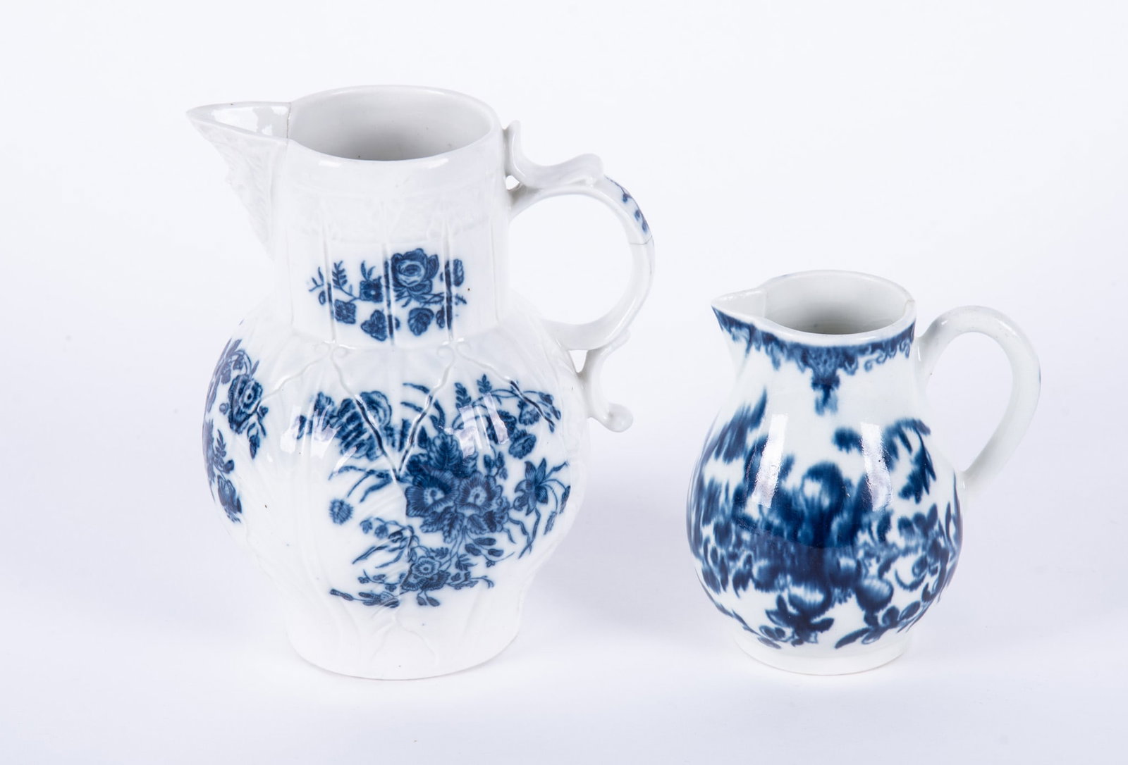 Two English Dr. Wall Period Porcelain Cream Jugs: England, 18th century, a rare Worcester creamer having a flowing blue botanical motif, 3 1/2 x 4 inches, bearing blue crescent mark to base, glaze bubble to back, tight hairline at rim extending to mi