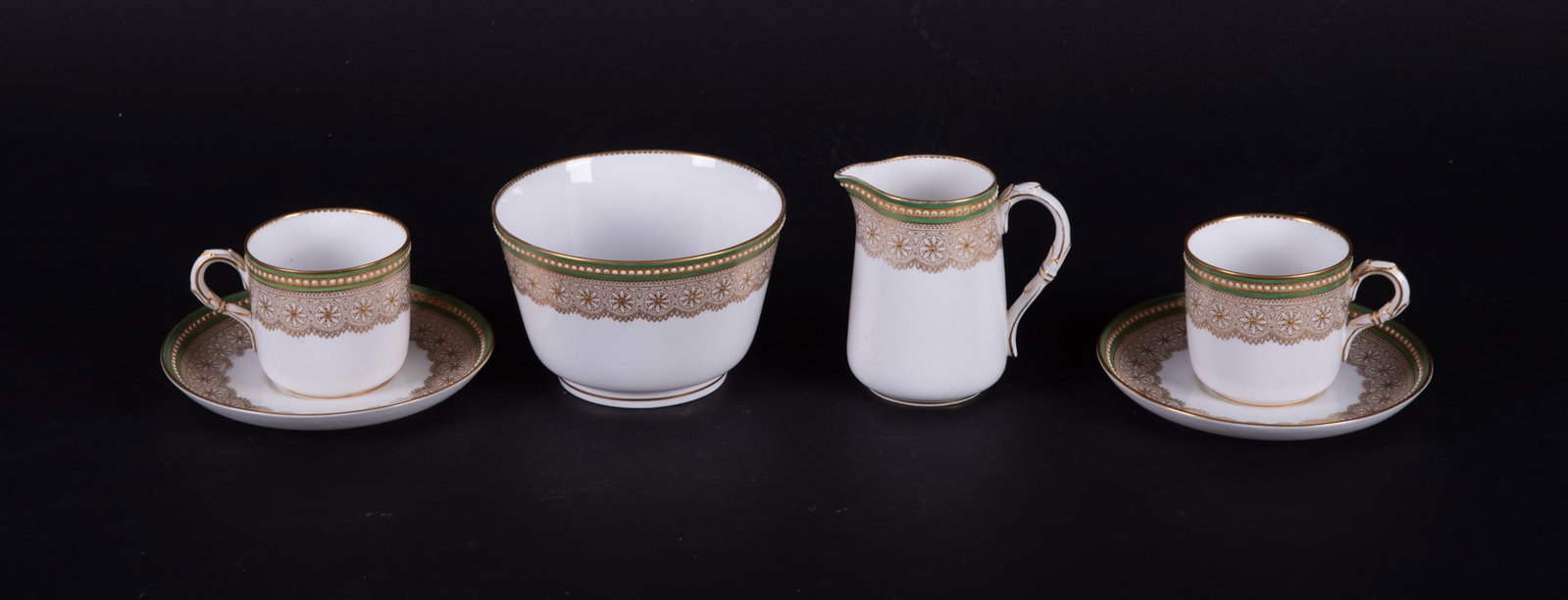 Four Royal Worcester Porcelain Gilt Jewel Table Articles: England, circa 1895, two cups/saucers, a creamer and large sugar or waste bowl, each piece with floral rosettes to the collar with fine gilt jewel beading, a green upper border with raised white ename