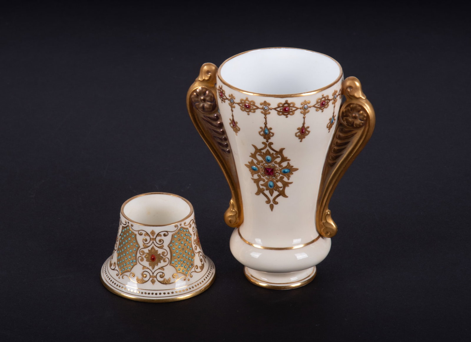 Two Jeweled Porcelain Coalport Table Articles: England, circa 1890, both pieces on a cream ground having gilt and enamel jewel highlights, the rare match holder alternating turquoise enamel gilt cartouches with red jewel ornament within sinuously 