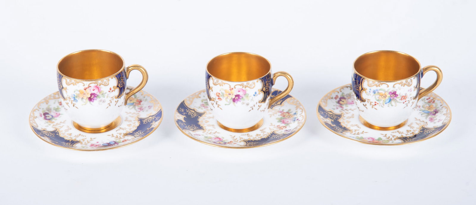 Three Matched Antique Coalport Porcelain Demitasse Cups and Saucers: England, circa 1900, 3 fine Coalport cups and saucers, the white ground painted in colorful floral designs with cobalt highlights, the interior of each cup gilt gold.