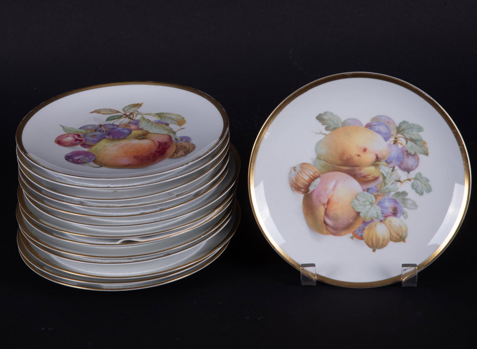 Two Bavarian Fruit or Desert Porcelain Plate Sets, PMR and Hutschenreuther: Bavaria, two very similar sets in the Orchard or Harvest patterns featuring fruits, nuts and vines, with wide gold rims. 8 of the plates by Hutschenreuther and 6 plates by PMR Bavaria Jaeger & Co.