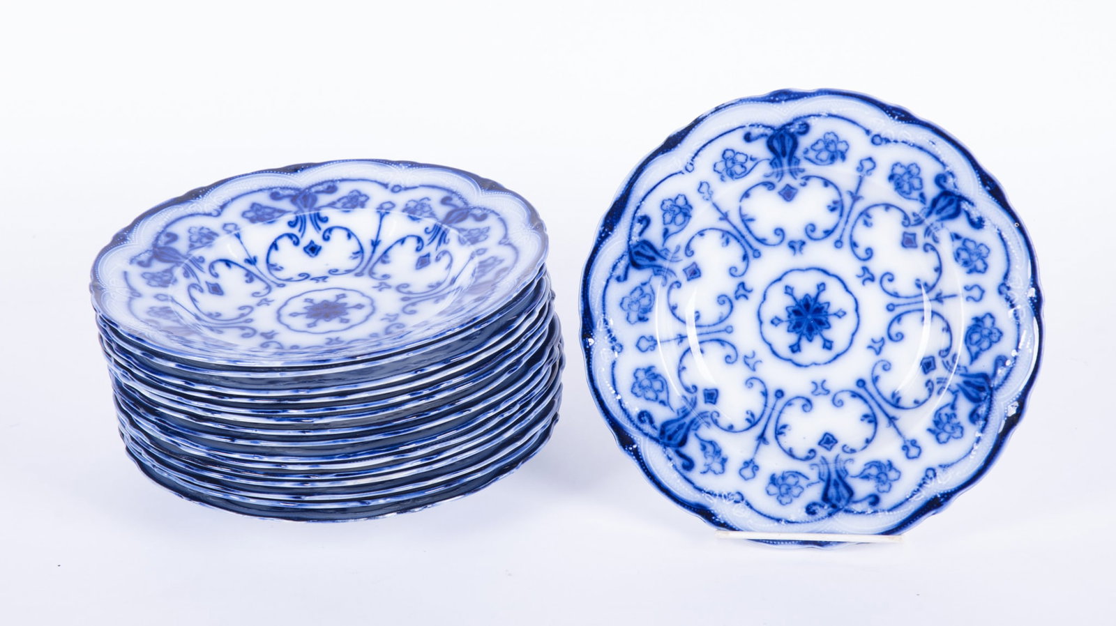 A Set of Sixteen Flow Blue Staffordshire Soup Bowls, Conway by New Warf Pottery: Burslem, England, circa 1890, a rarely found set of 16 soup bowls in the Conway pattern. Produced roughly from 1878-1894, the pattern features a stylized floral and geometric design that transitions f