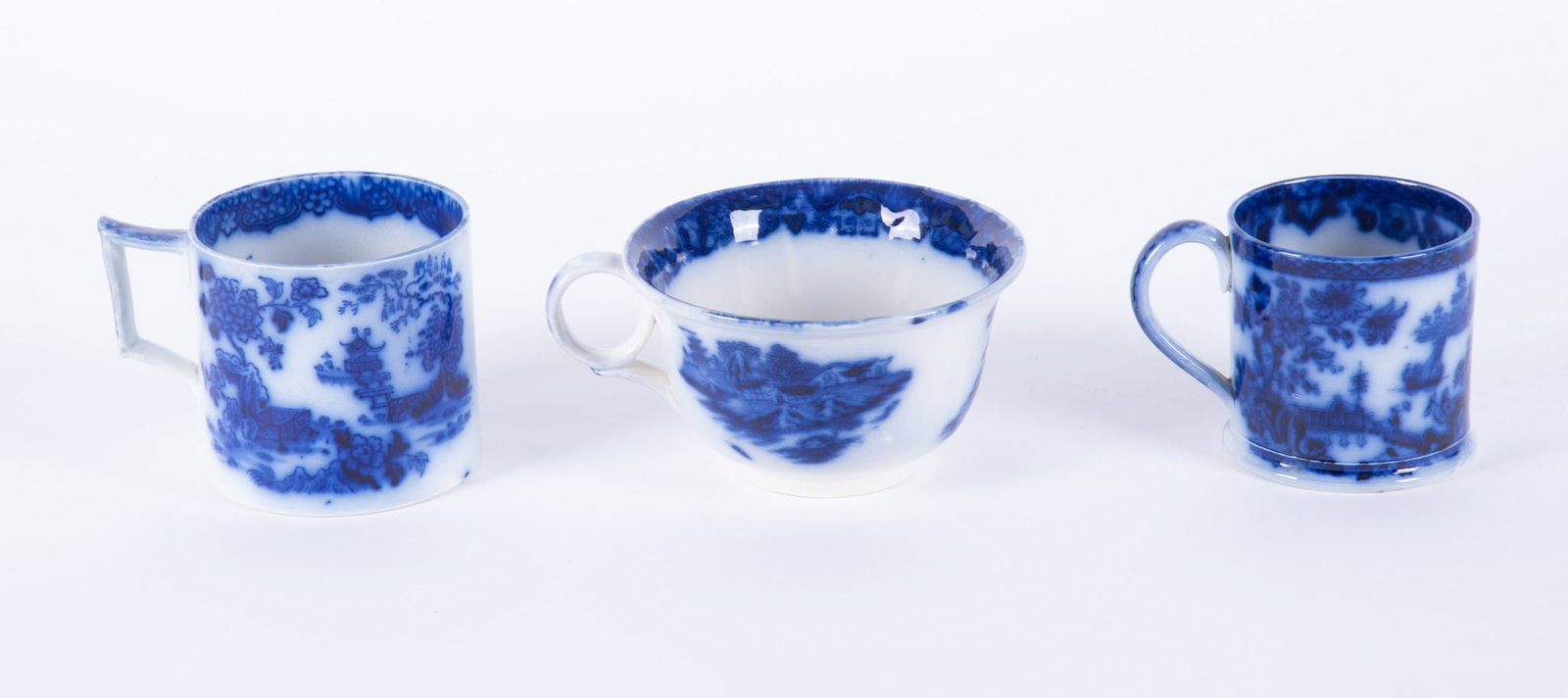 Three Staffordshire Chinoiserie Style Flow Blue Coffee Mugs: England, mid-19th century, all three deep flow blue handled coffee mugs or cans having an Asian influence design.