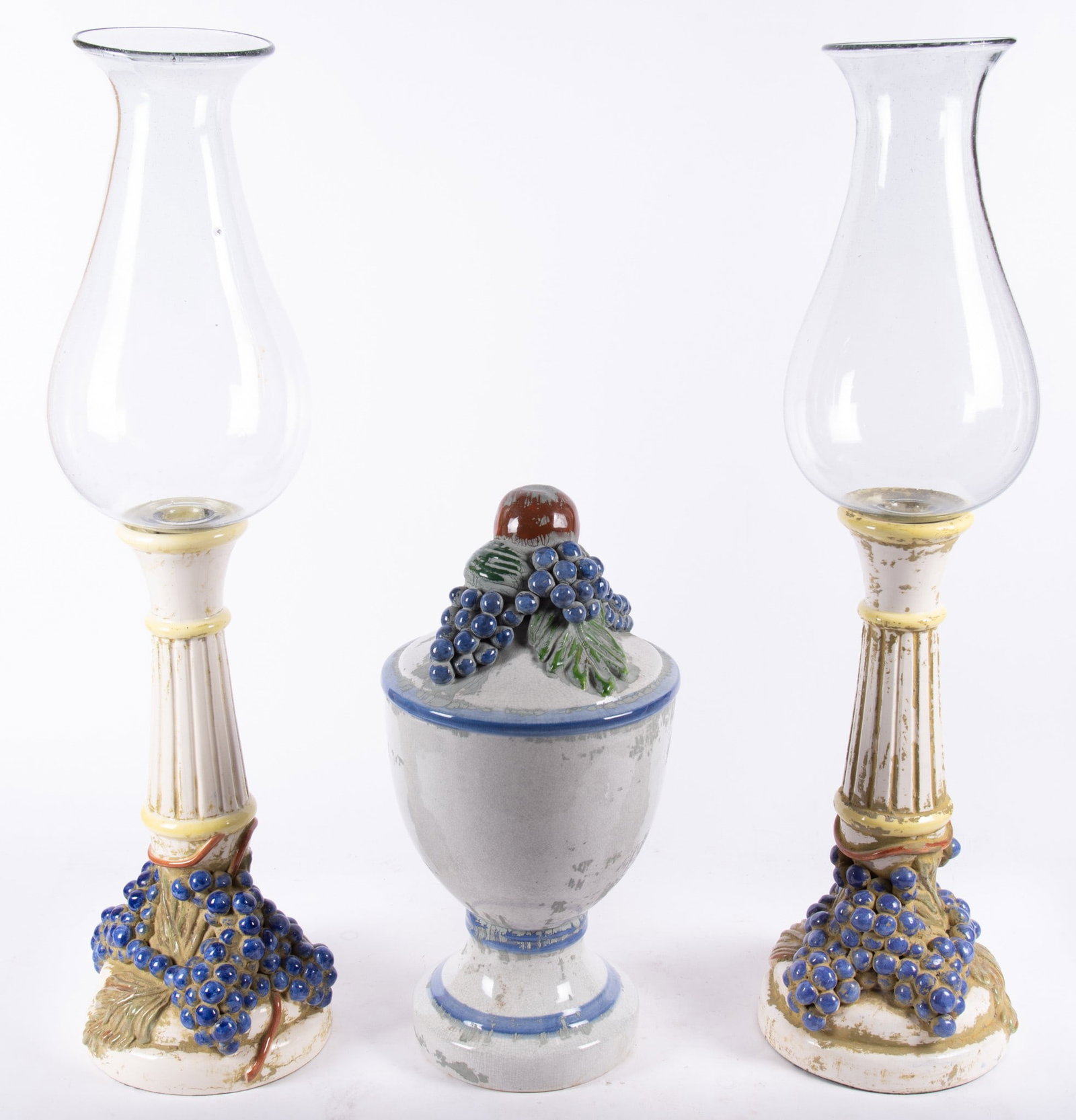 Majolica Style Porcelain Table Garniture with Hand Blown Hurricane Style Shades (3 pieces): pair of bases with tapering fluted column, heavily detailed grapes, leaves and vines, center urn with crackle glaze and also with grape motifs and apple.