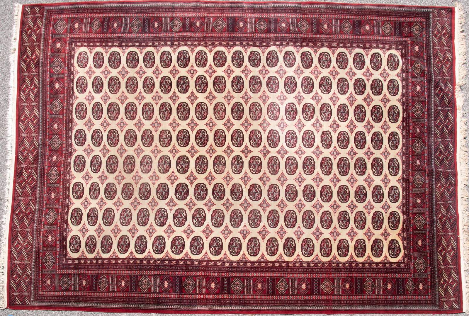 Handwoven Persian Bokhara Room Rug: Handwoven Persian Bokhara Room Rug Ivory field with a repetitive "elephant foot" motif pattern centering a primary border and multiple guard borders. 9' 7" x 12' 7"