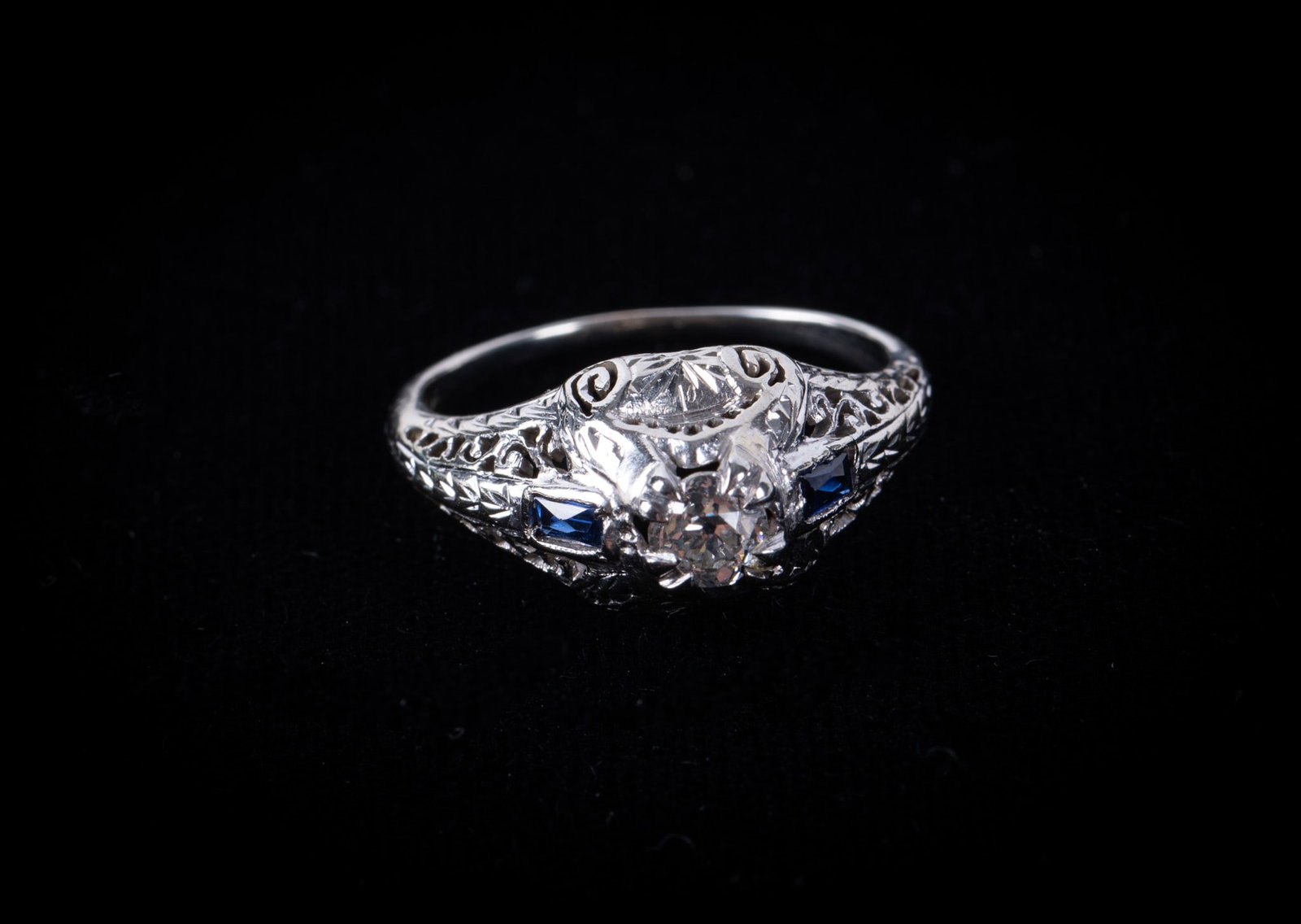18K White Gold Filigree Diamond & Sapphire Art Deco Ring: 18K White Gold Filigree Diamond & Sapphire Art Deco Ring This Art Deco ring has an approximate quarter carat center diamond with a sapphire baguette on each side. The mounting sets high which adds to 
