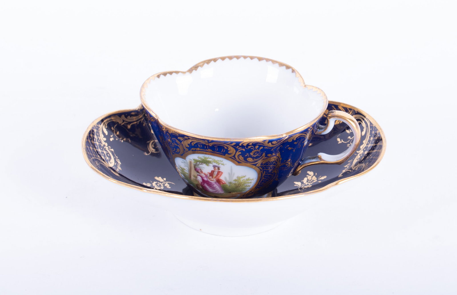 A German Cobalt and Hand Painted Cabinet Cup and Saucer: A German Cobalt and Hand Painted Cabinet Cup and Saucer Dresden, circa 1900, a finely detailed quatrefoil-shape cup and saucer having a cobalt blue ground with gilt highlights and panels of amorous co