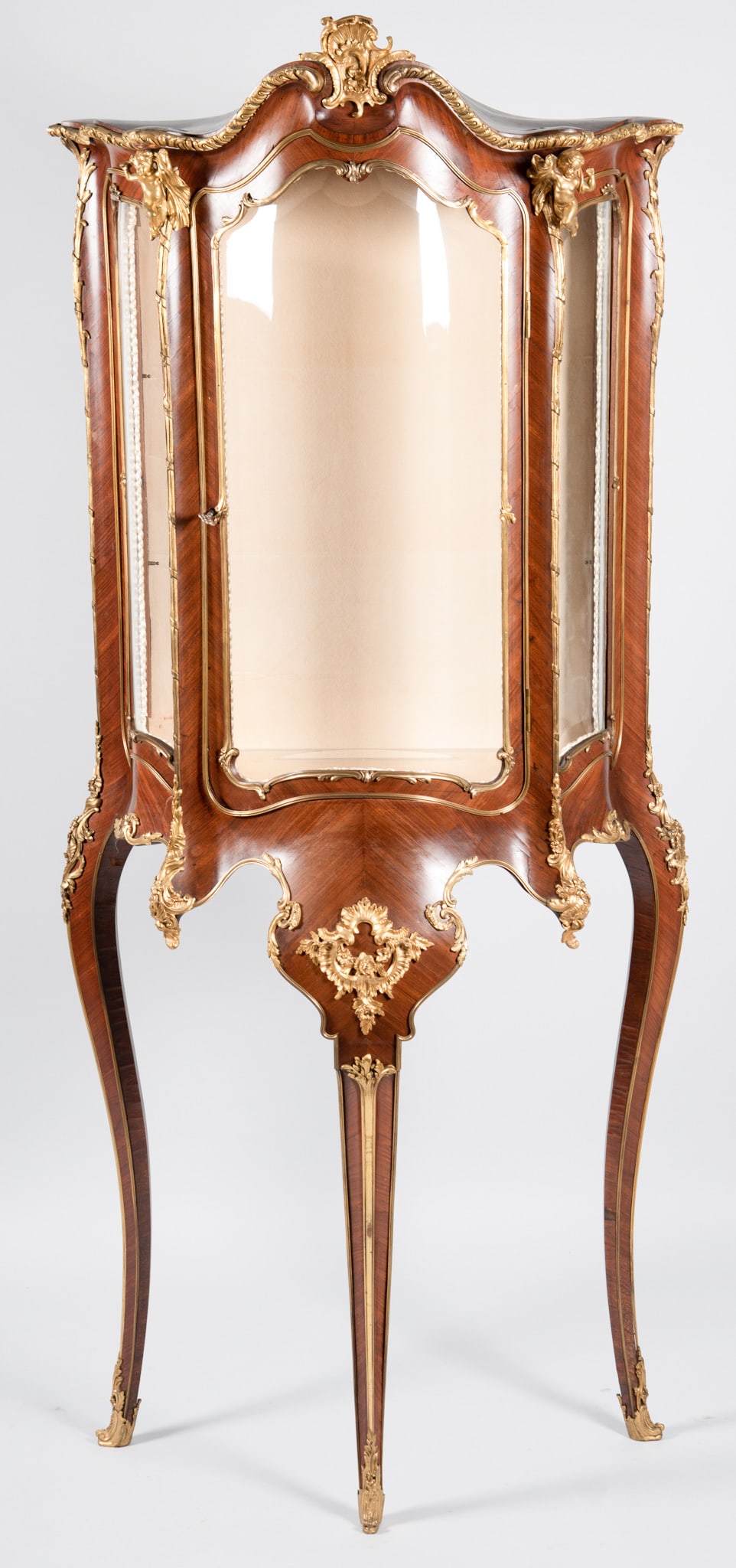 Karges French Louis XV Vitrine Cabinet: Karges French Louis XV Vitrine Cabinet Ormolu crest above a serpentine glass door centering a pair of gilt bronze cherubs all above a elaborate apron with scrolling bronze mounted designs ending on
