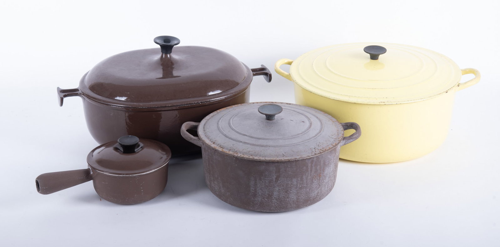 Four Pieces of Vintage Le Creuset Cookware: Four Pieces of Vintage Le Creuset Cookware Including Lemon Yellow, Brown, and Weathered Dutch Ovens, and a brown Sauce Pot. Largest: 8 x 15 x 13 inches