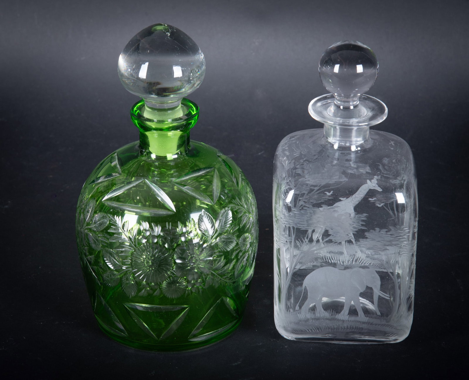 Emerald Green Cut to Clear Crystal Decanter along with an Intaglio Cut African Scene Decanter: Emerald Green Cut to Clear Crystal Decanter along with an Intaglio Cut African Scene Decanter The emerald decanter has a floral motif with a clear dome shaped stopper. It is 8 1/2 inches tall. The cle
