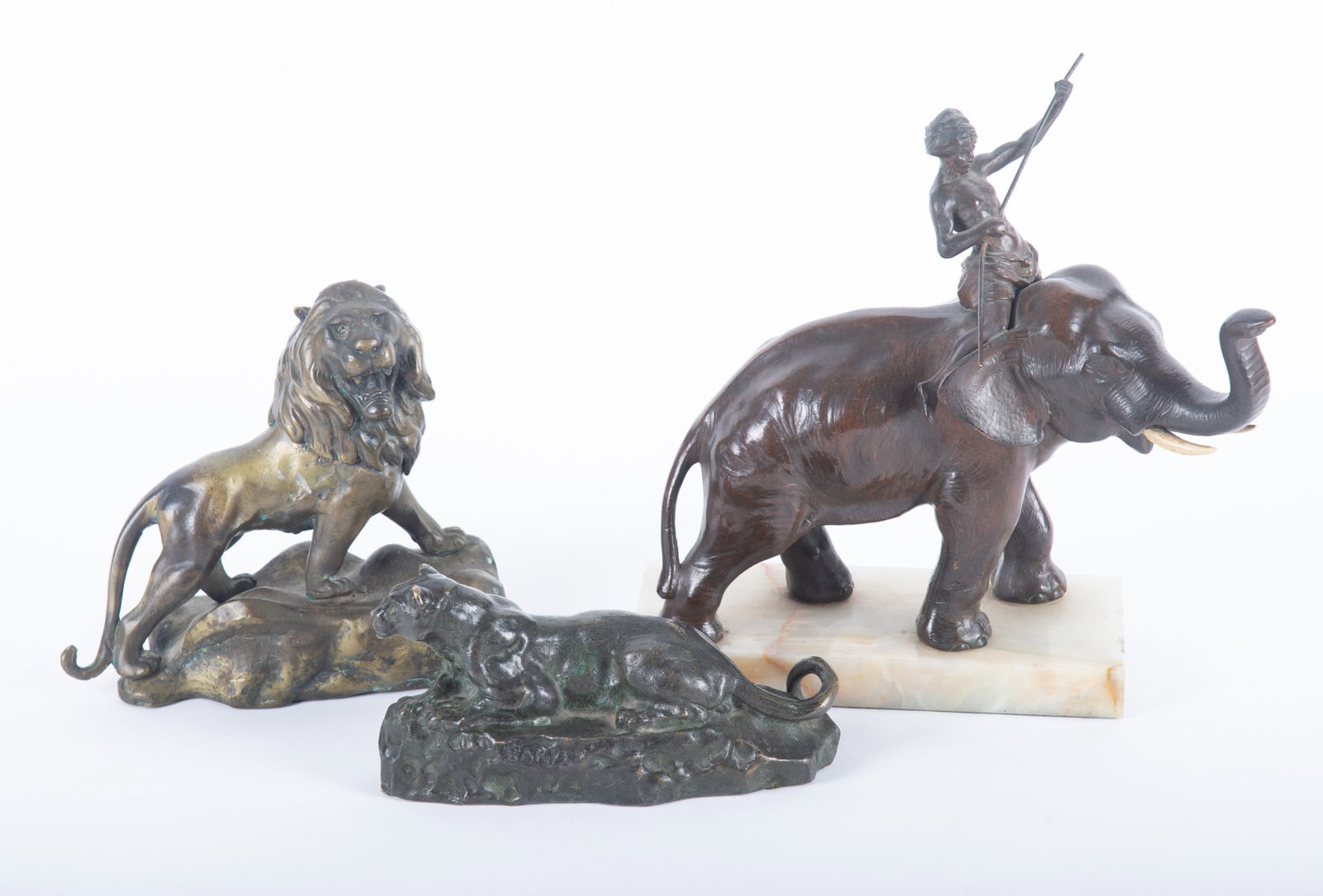 A Group of Three Animalier Sculptures: A Group of Three Animalier Sculptures A bronze of a recumbent Lioness, signed and after Bayre; and unsigned bronze of a standing Lion perched on a boulder; and a bronzed metal figure group of an eleph