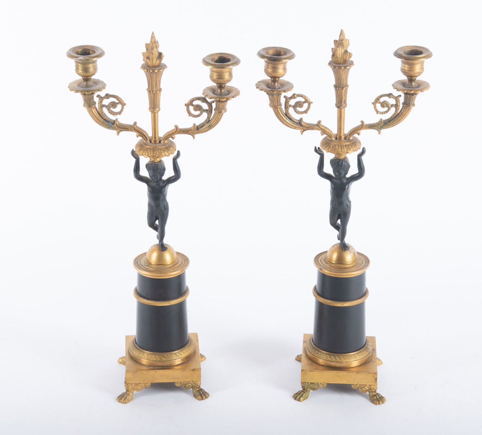 A Pair of French Empire Style Gilt and Patinated Bronze Candelabra: A Pair of French Empire Style Gilt and Patinated Bronze Candelabra France, late 19th/early 20th century, a pair of bronze 2-arm candelabra, the central column raised on paw feet, supporting a young Ba