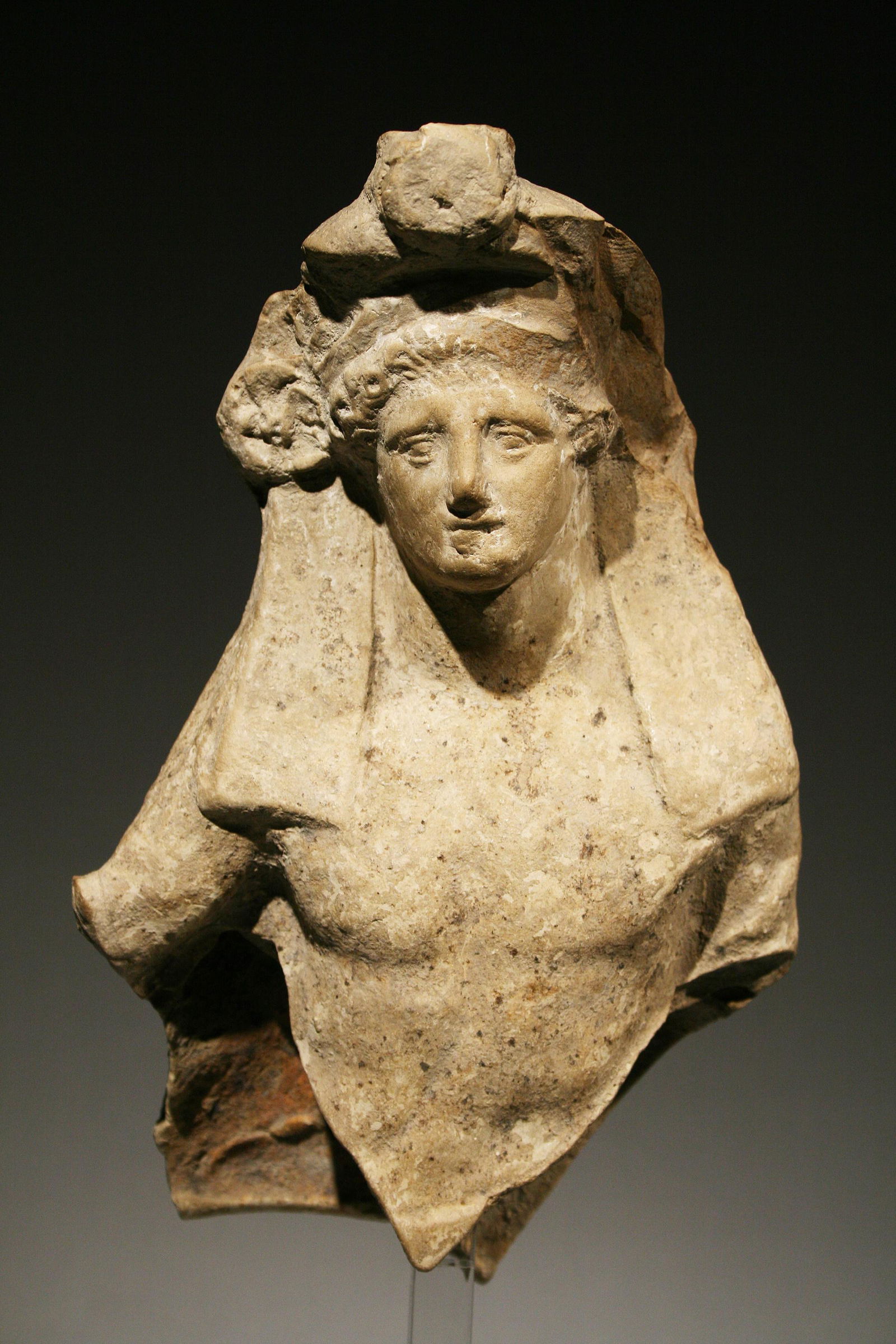 A Symposiast: Western Greek ca. 340 B.C.. Terracotta. H. 20 cm. W. 12 cm Upper body of a symposiast. The beardless youth reclines to right. His head is adorned by a broad fillet as well as an opulent wreath with ro