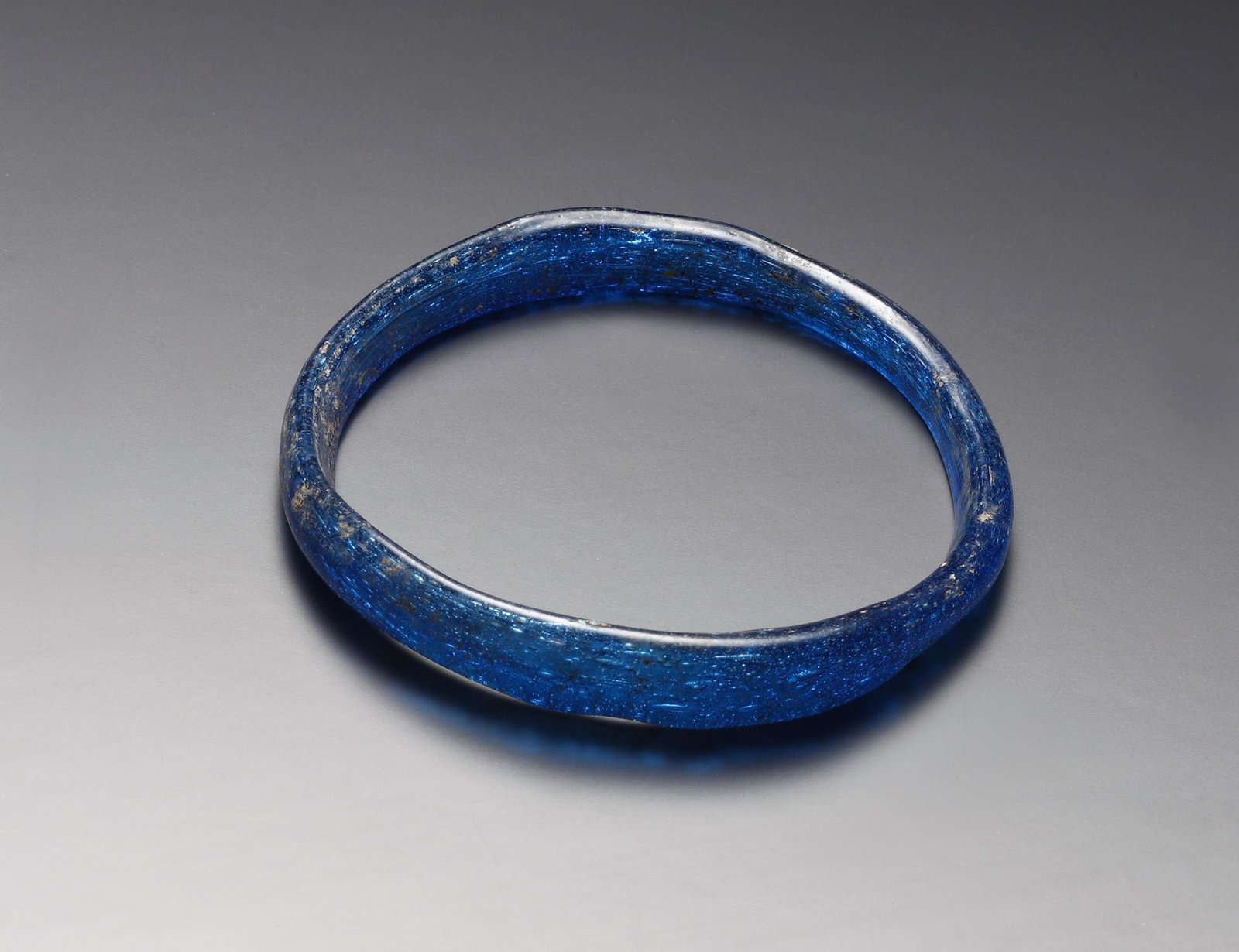 A Bracelet: Roman to Islamic 1st-4th cent. A.D. or later. Blue translucent glass. Dm. max. 5.5 cm Bent out of a single strand of glass, the place where the two ends meet being slightly thicker. Condition: Intact.