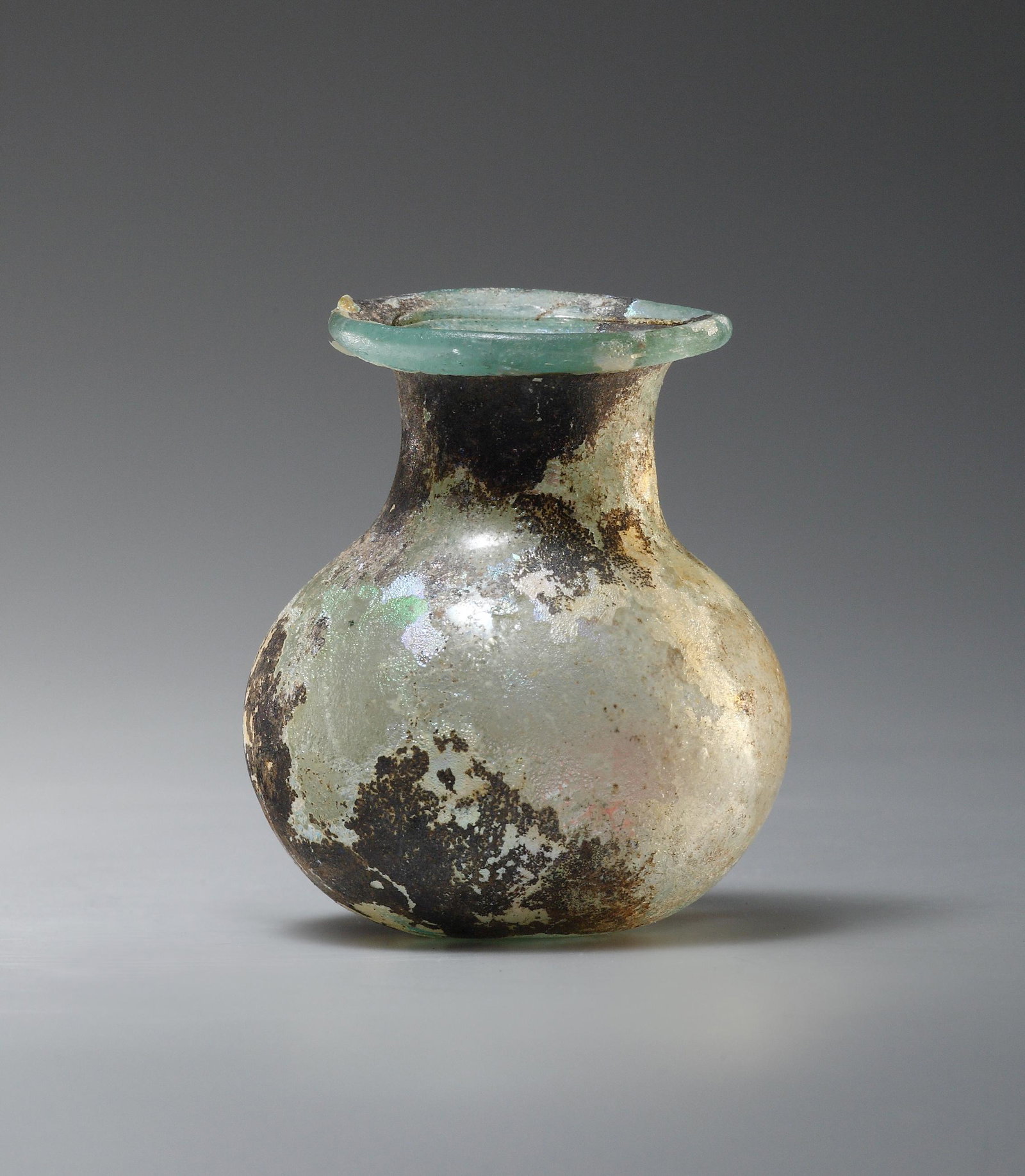 A Spherical Bottle: Roman, Eastern Mediterranean 4th-5th cent. A.D.. Greenish glass. H. 5.8 cm. W. max. 4.7 cm The spherical body transitions softly into the neck. Rim folded inwards. Condition: Iridescent. Intact. With