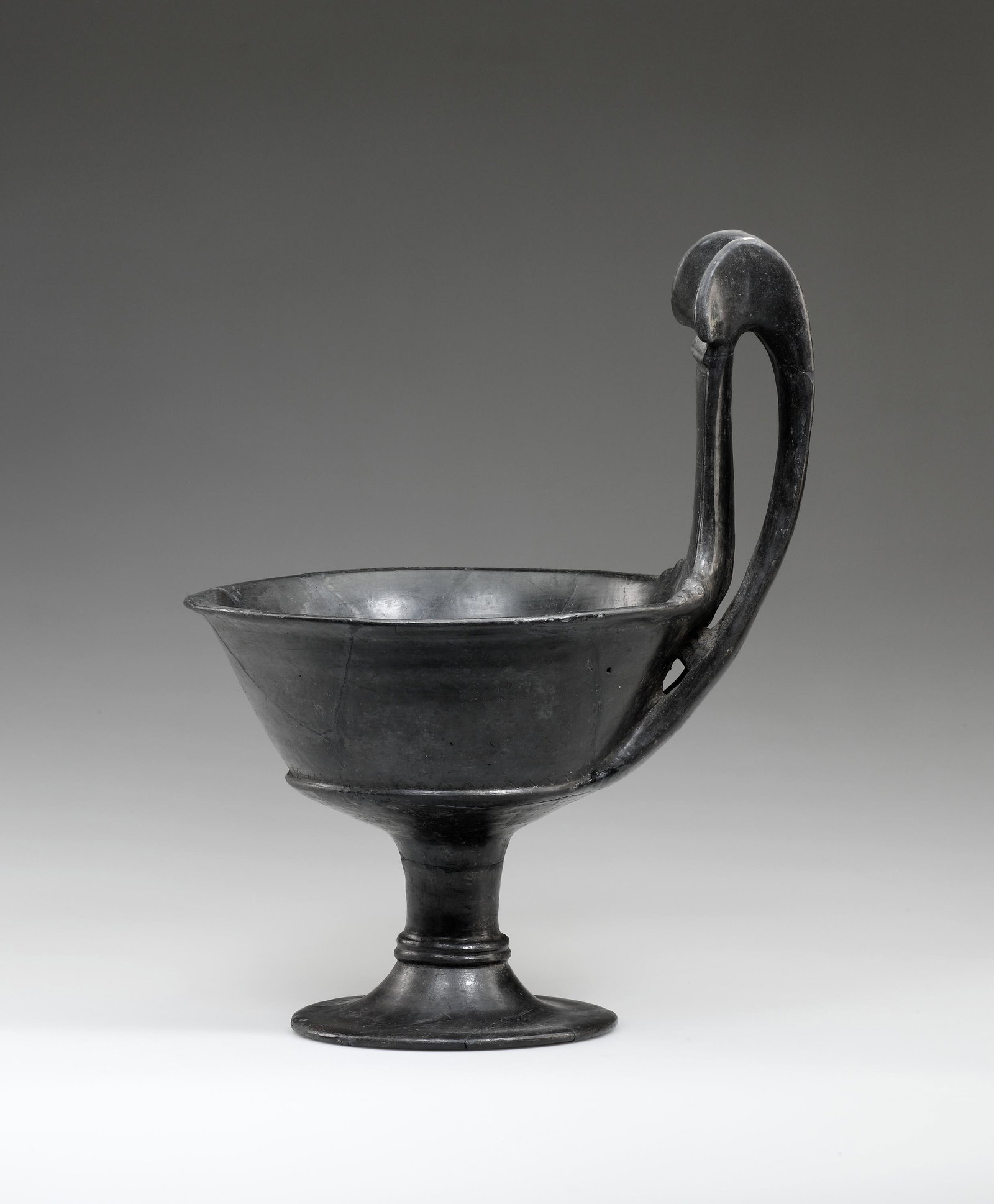 A Monumental Etruscan Bucchero Kyathos: Etruscan 2nd half of 6th cent. B.C. Clay. H. 37.5 cm (with handle); 27 cm. (excluding handle). A monumental chalice-shaped vessel in "bucchero pesante” with a deep, flaring cup and broad, high strap