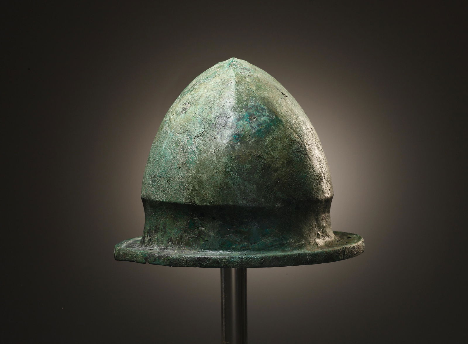 A Negau Helmet (Vetulonia Type): Italic late 6th-1st half 5th cent. B.C. Bronze. H. 19 cm. W. max. 23.6 cm. D. max. 26.7 cm. Compact bronze helmet whose closed crown rises up to a sharp medial ridge; two holes at the top to the left