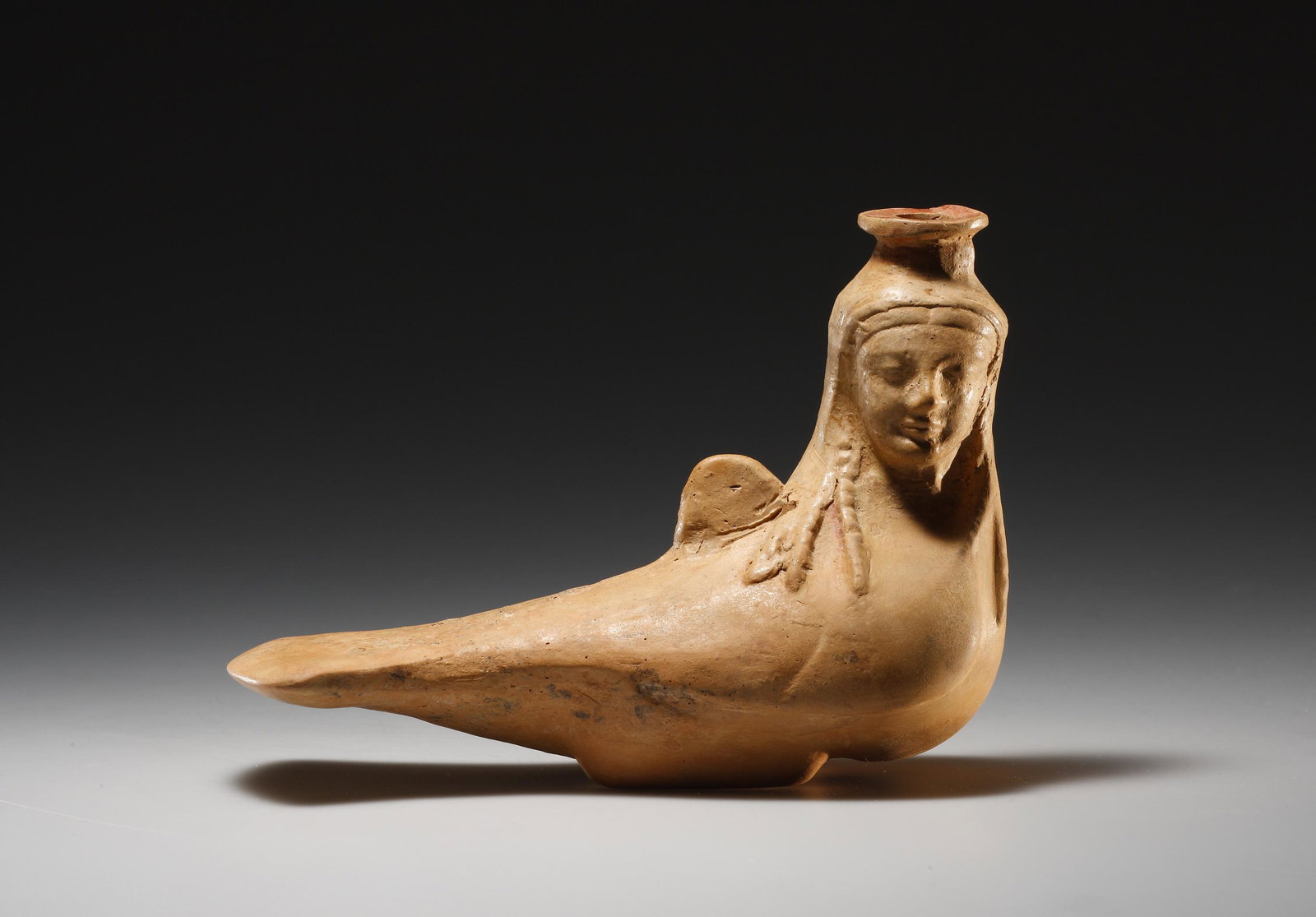 A Rhodian Askos in the Form of a Siren: Rhodian 2nd half of the 6th cent. B.C. Clay. L. 15.7 cm. Formed of buff clay, this askos (flask) is in the shape of a siren - a mythological hybrid creature combining the head and upper torso of a you