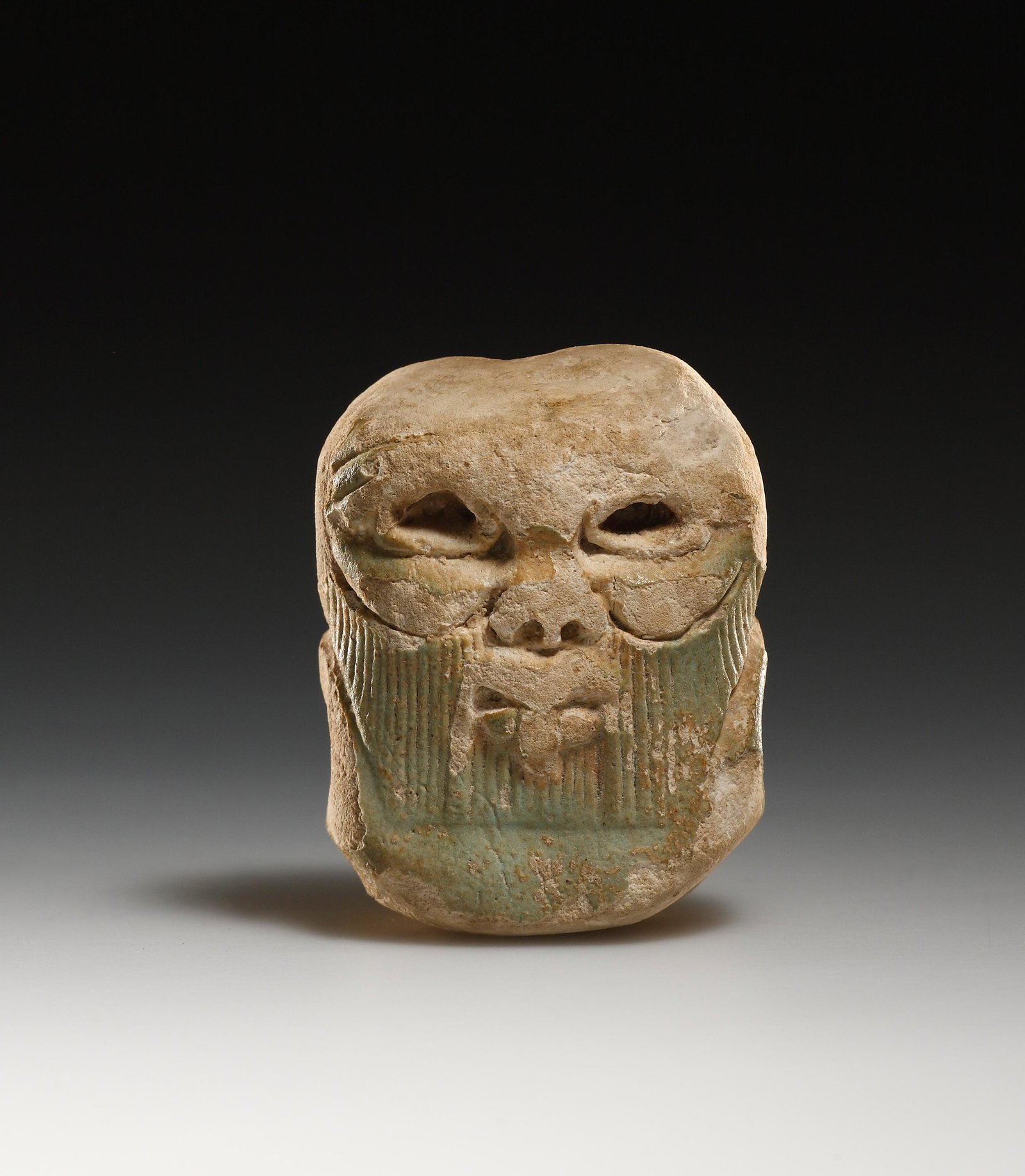 A Head of the God Bes: Egypt Third Intermediate Period, 1100-650 B.C..Faience. H. 4.2 cmA head of the Egyptian god Bes. Constructed from fired faience, some preserved blue is found on the beard and on the back of the head. 