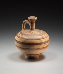 A Late Mycenaean Jug: Late Myceneaen 12th cent. B.C..Clay. H. 12 cm. A small jug with flaring body tapering into a low ring foot. Tubular vertical spout. Single handle connecting to nearly horizontal shoulder which is