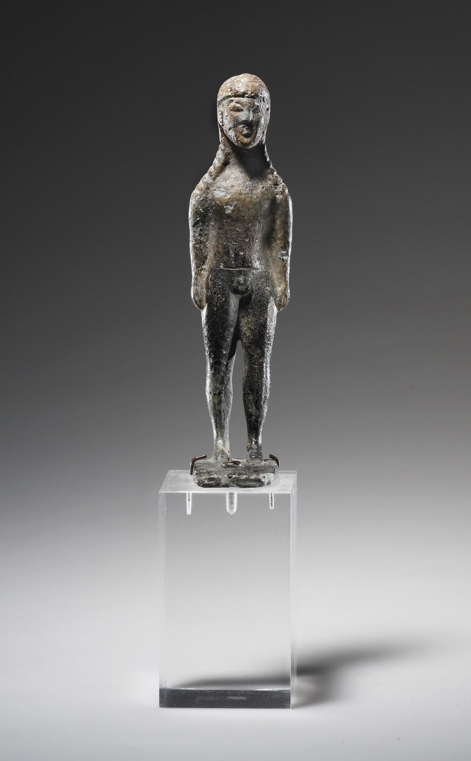 A Statuette of a Kouros: East Greek mid 6th cent. B.C..Bronze. H. 10.9 cmThe nude youth stands frontally on a square plinth in the static pose typical of kouroi. His arms hang straight down and his hands rest against his thig