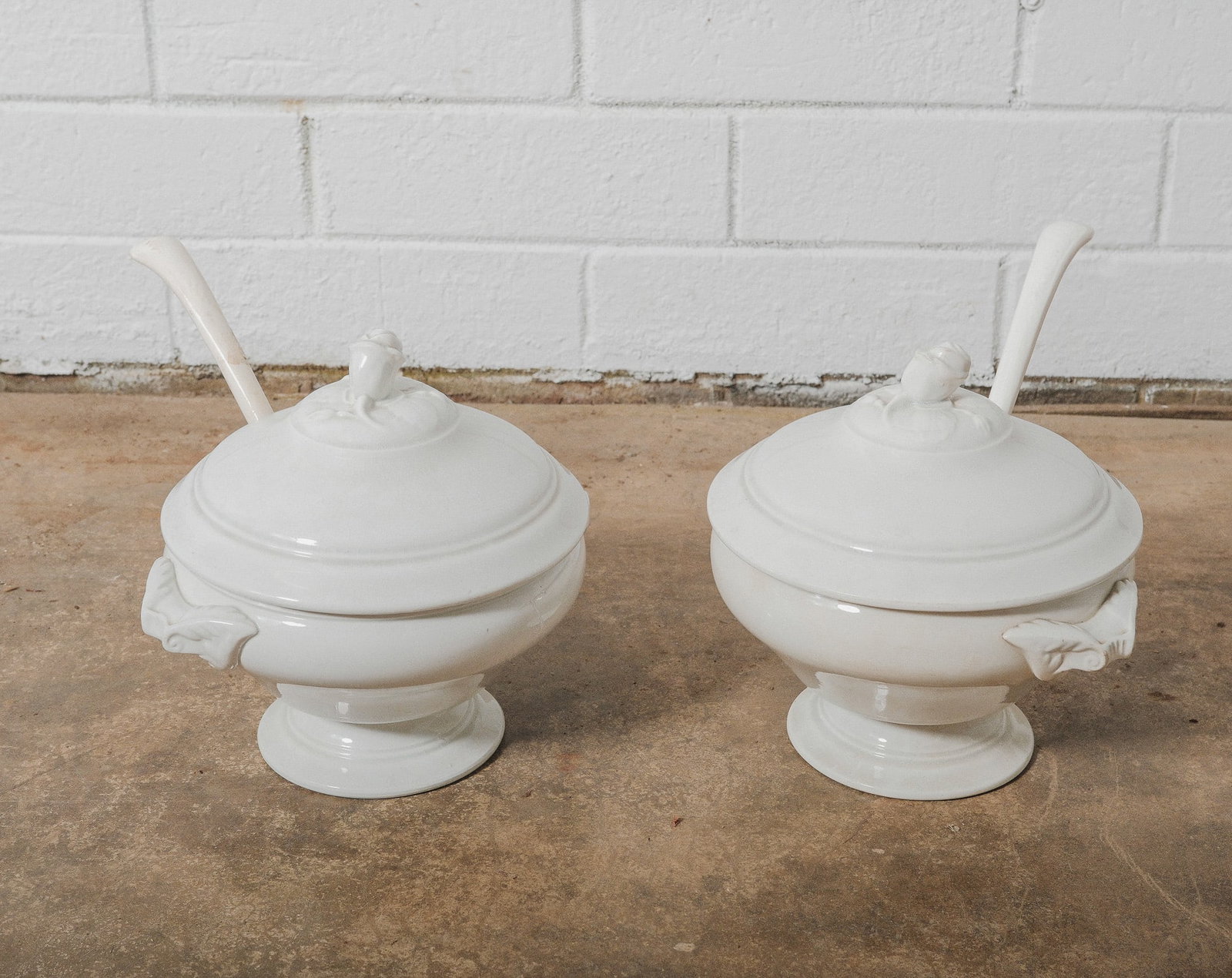 Belgium Ironstone Covered Soup Tureen with matching Ladle, one pair: Pair of white glazed stone wear soup tureens, each featuring an elegant pedestal base, matching domed lids, and sculptural rosebud finials. The side handles are shaped with figural detailing. Each tur