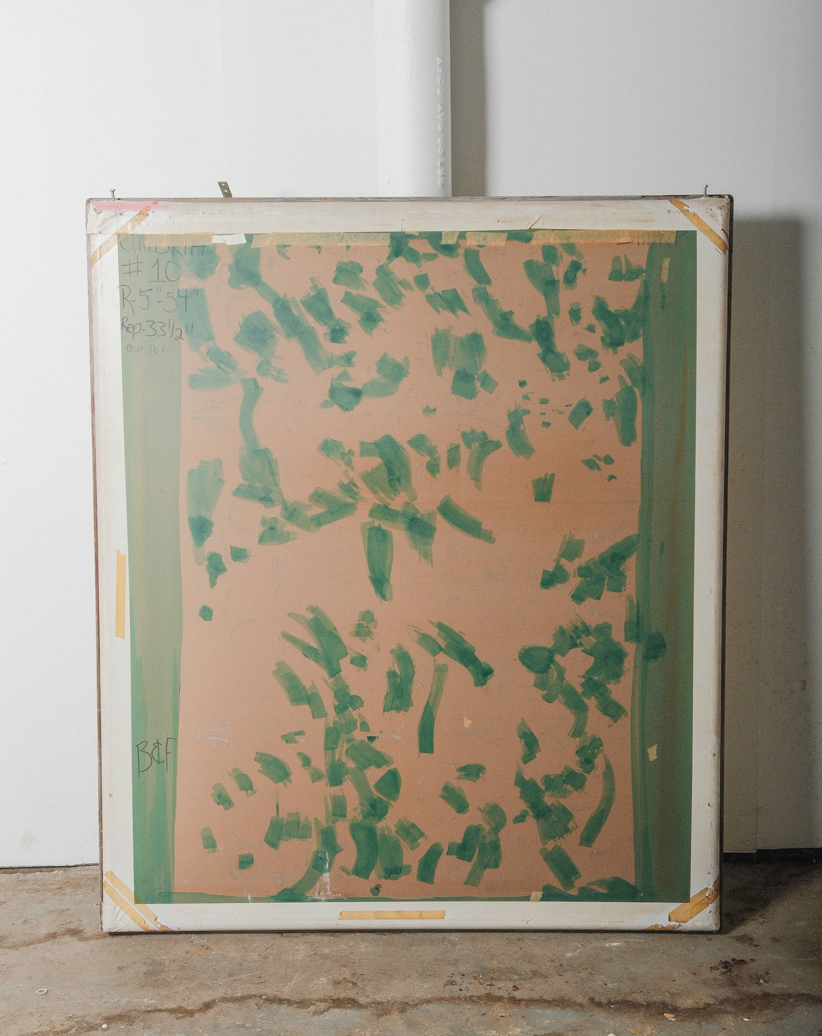 Vintage Silk Screen Printing Frame with Abstract Green on Mesh: A vintage silk screen printing frame features a vivid abstract pattern in green pigment over a peach toned mesh. Likely used in textile or wallpaper production, the screen displays bold brush strokes