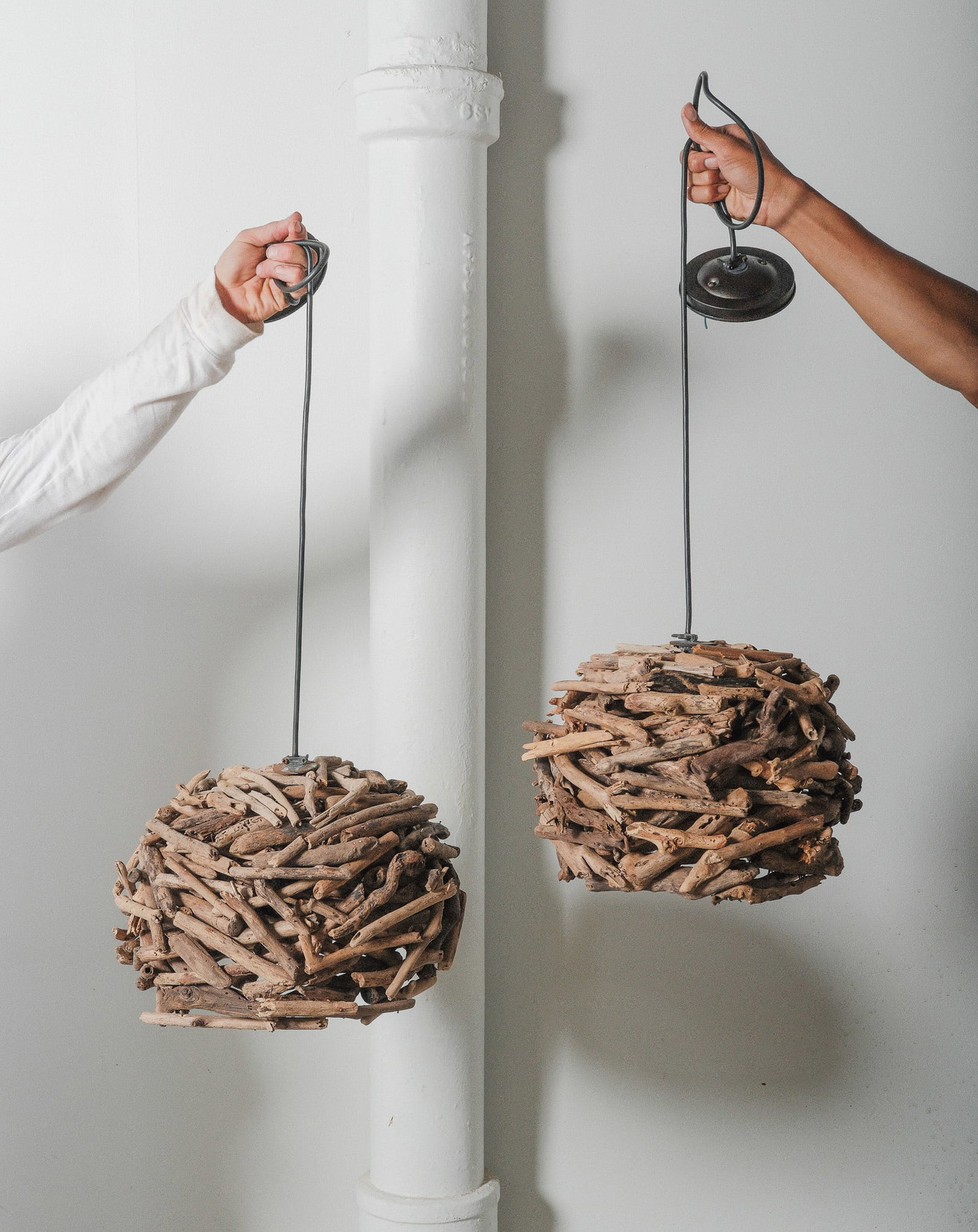 Pair of Driftwood Pendant Lights: A unique pair of handcrafted pendant light composed on intricately woven driftwood pieces forming a spherical shape. These sculptural light fixtures showcase the raw beauty of the natural drift wood, 