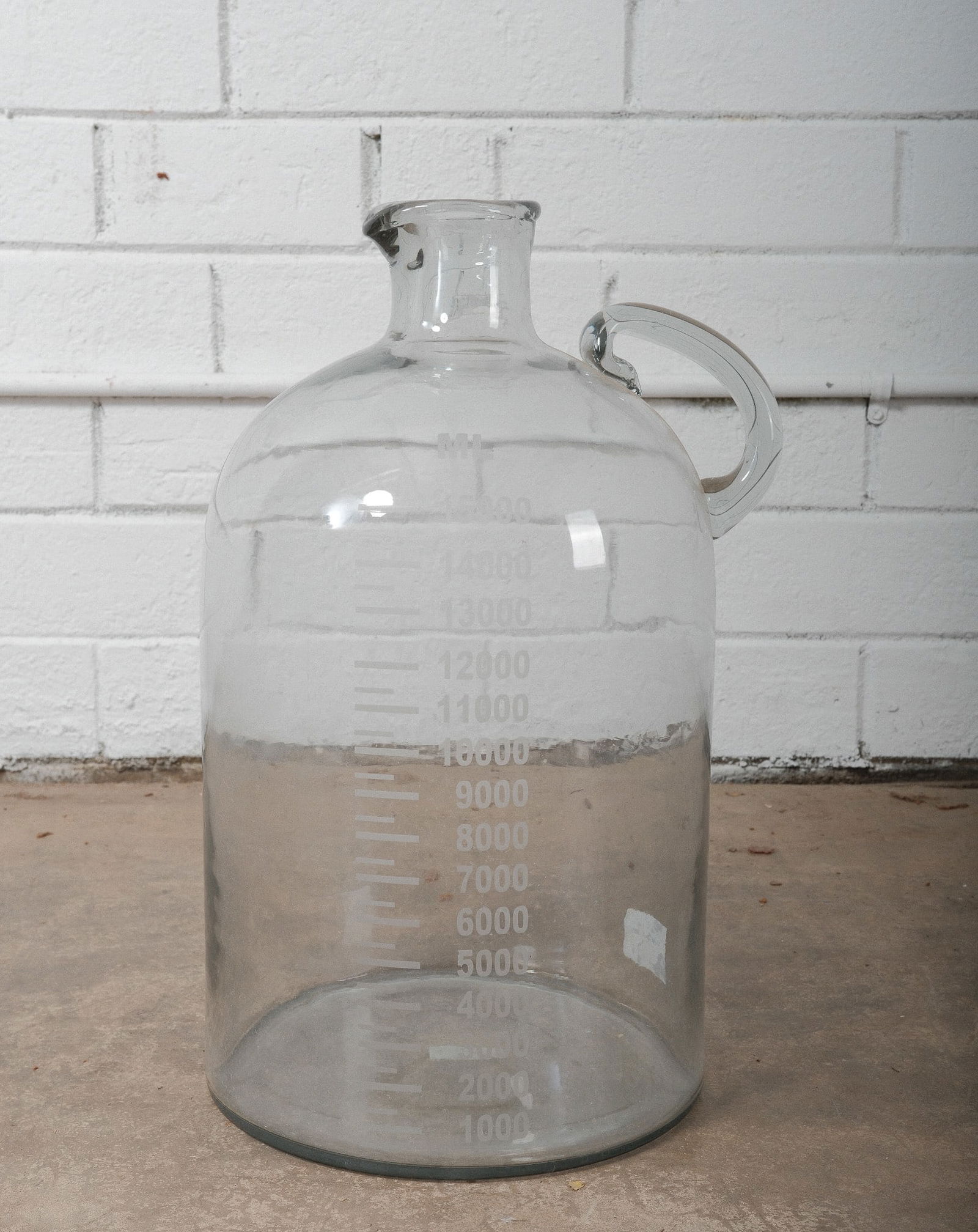 Clear Glass Laboratory Demijohn Bottle: A classic vintage clear glass carboy bottle featuring a rounded body with straight sides, a short neck with a wide mouth, and a looped glass handle.